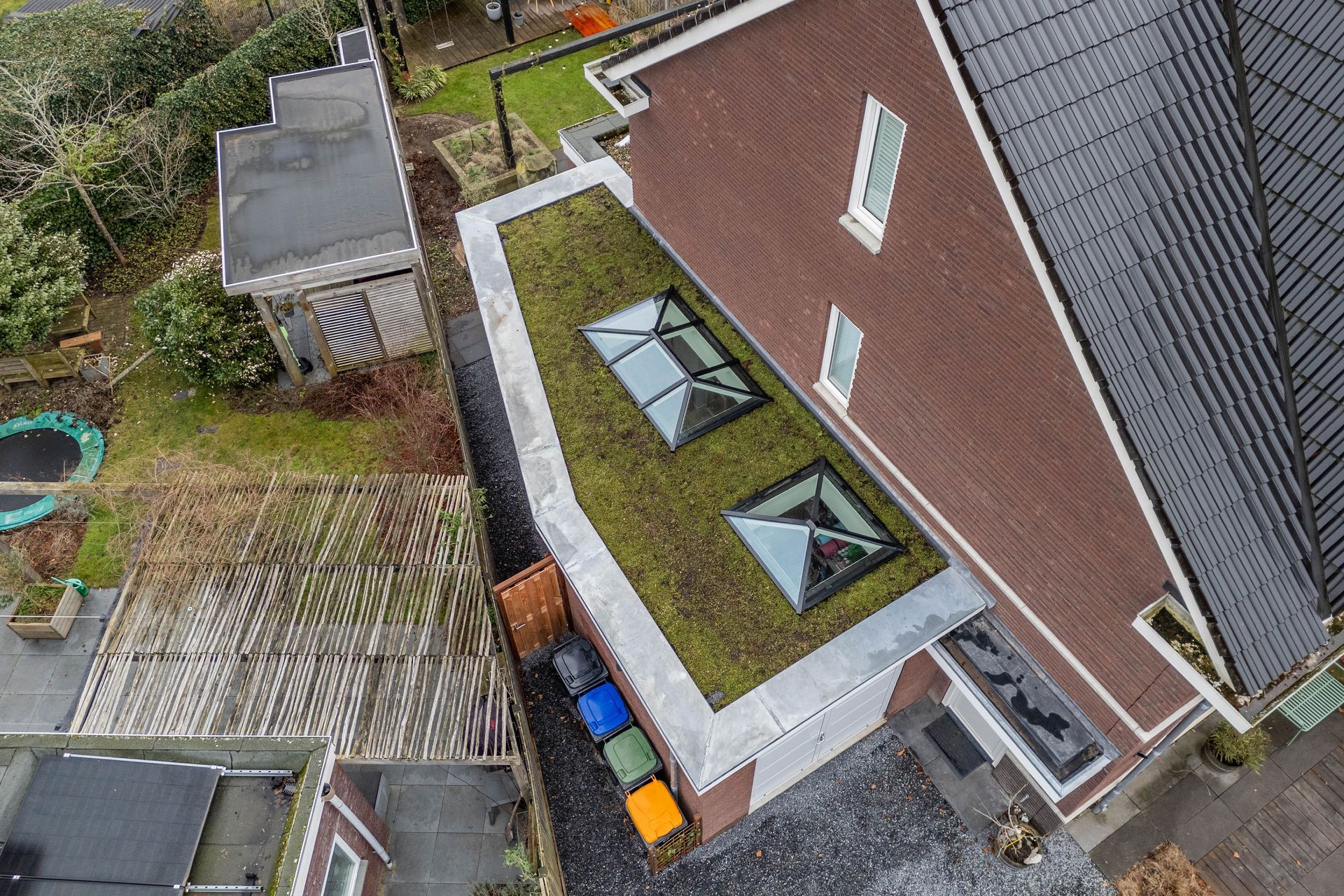 Luchtfoto van een huisdak met twee dakramen en daaronder een klein terras in de achtertuin.