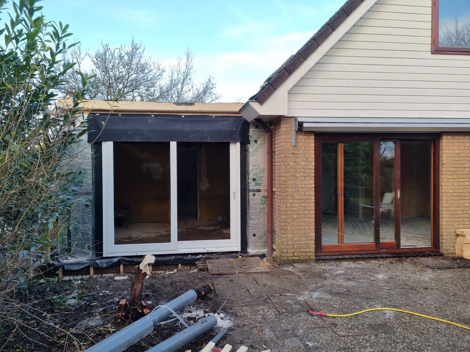 Aanbouw met zwarte ramen in constructie. Verbouwing aanbouw en renovatie deuren.