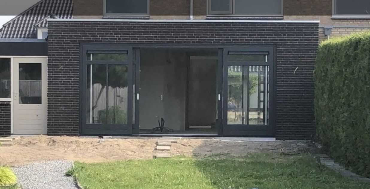 Aanbouw met donkergrijs gevel verbouwing. Moderne schuifdeuren en ramen gerenoveerd.