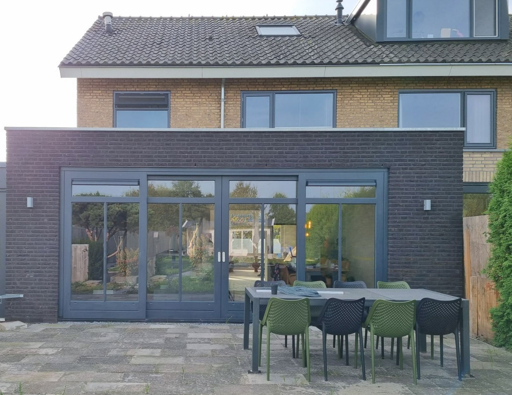 Moderne aanbouw met donkere gevel. Verbouwing woning met veel ramen.