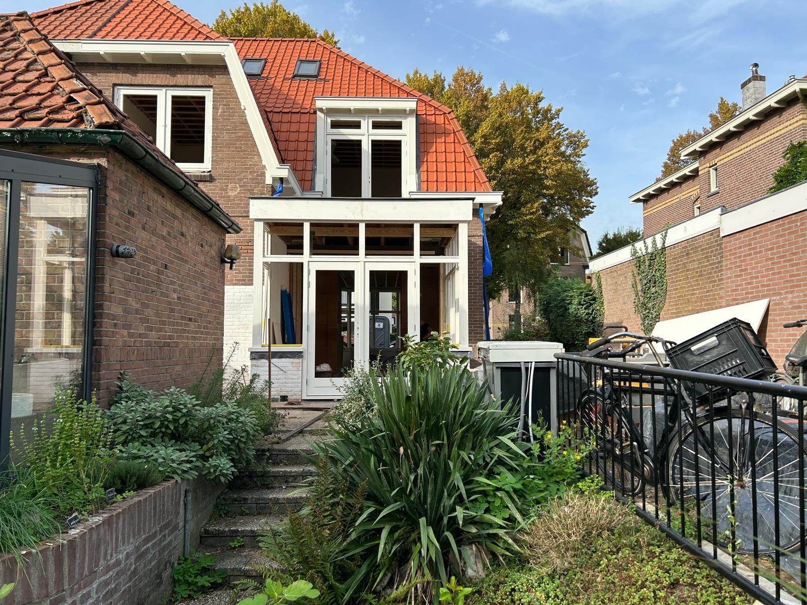 Bakstenen huis met rode dakpannen. Witte houten veranda uitbouw. Moderne verbouwing woning.