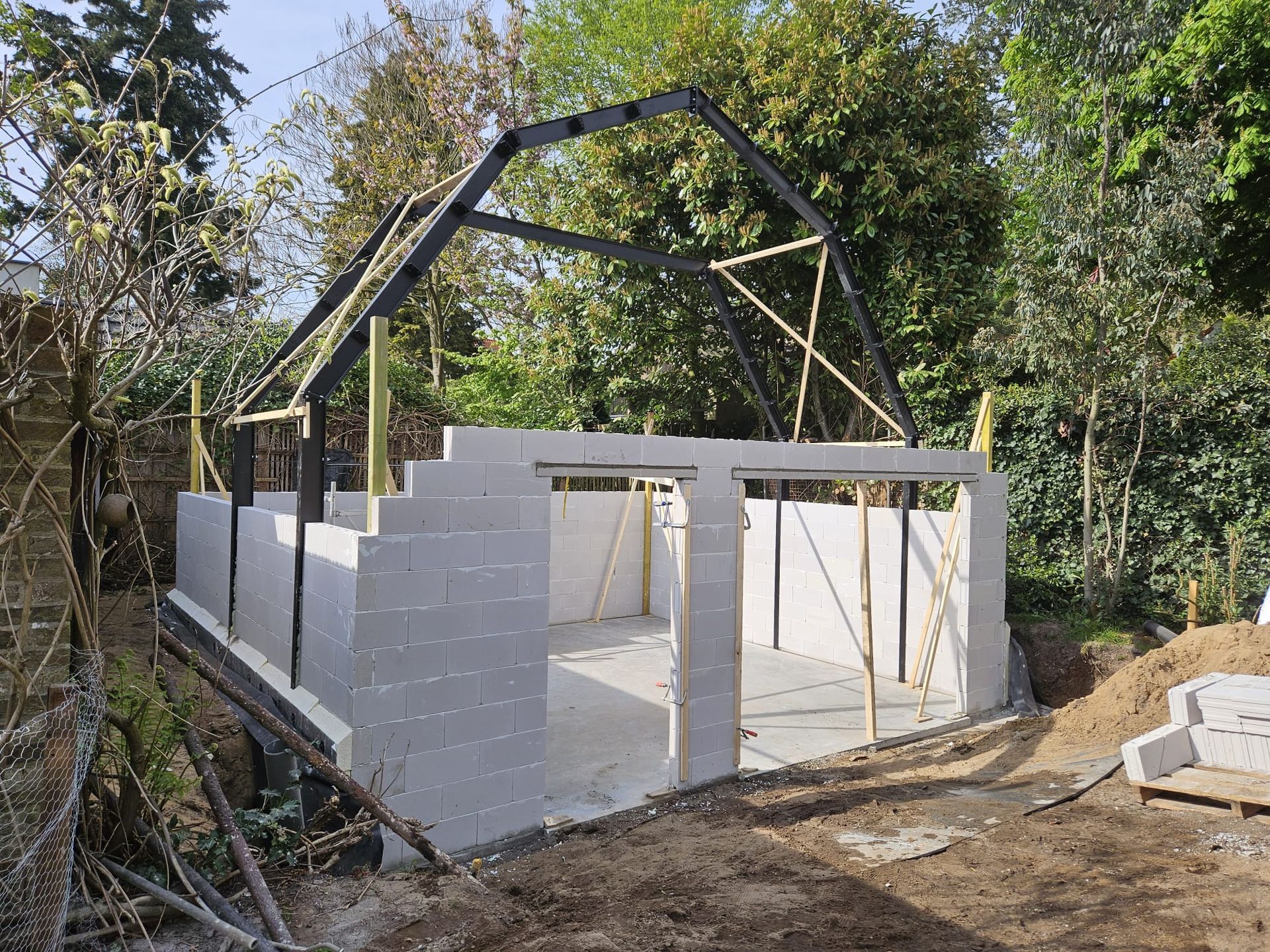 Gedeeltelijk gebouwd wit stenen huisframe met houten dakspanten in een bosrijk gebied