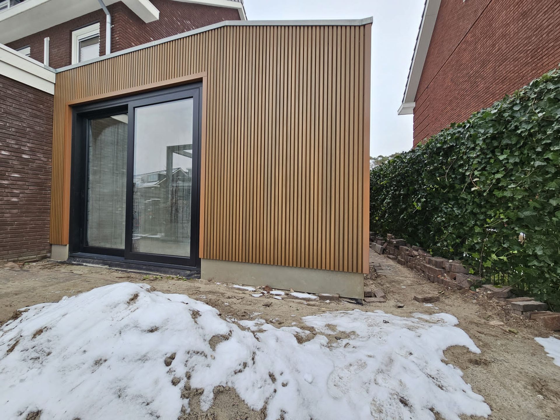 Houten aanbouw met moderne glazen deuren. Woninguitbouw en aanbouwwerk aannemer.