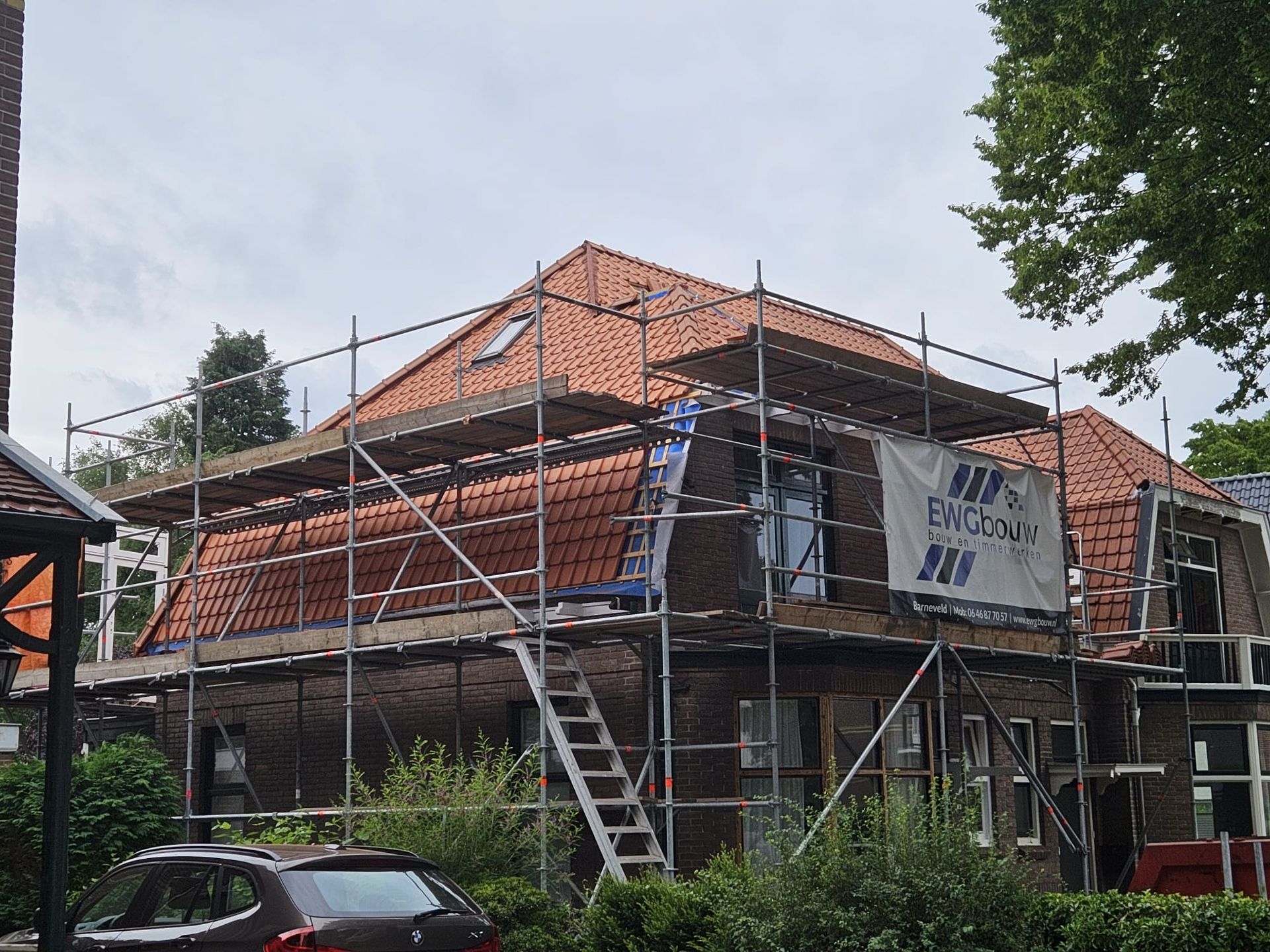 Dakwerk in aanbouw met steiger. Dak renovatie en baksteenwerk. Aannemer werkzaamheden zichtbaar.