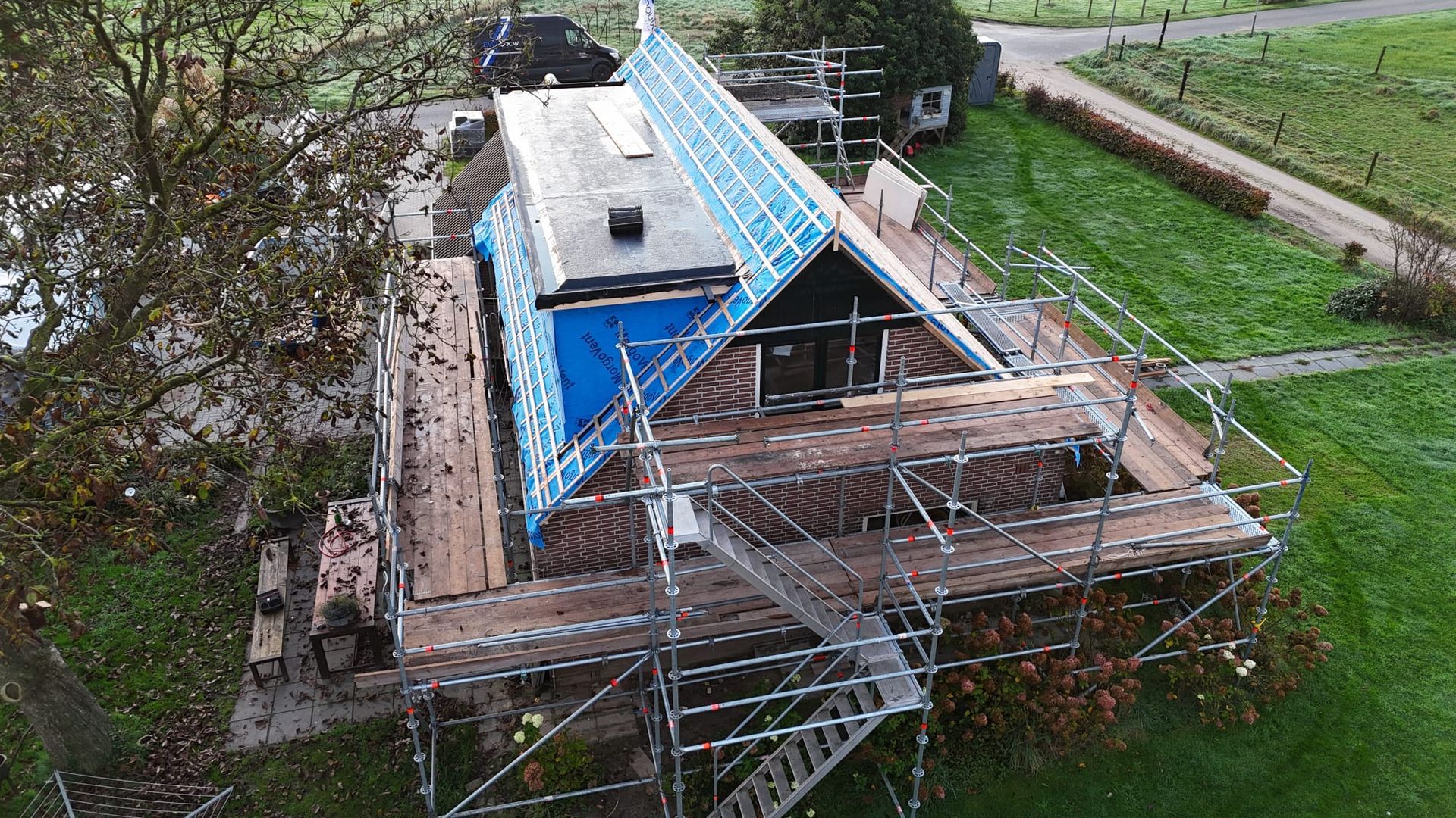 Woning dakwerk met blauwe bescherming en steiger. Dakrenovatie en bouwsteiger.
