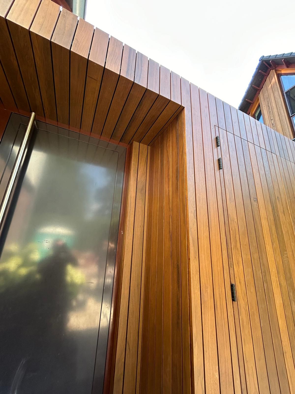 Moderne houten gebouwingang met verticale lamellen en een deur van matglas.