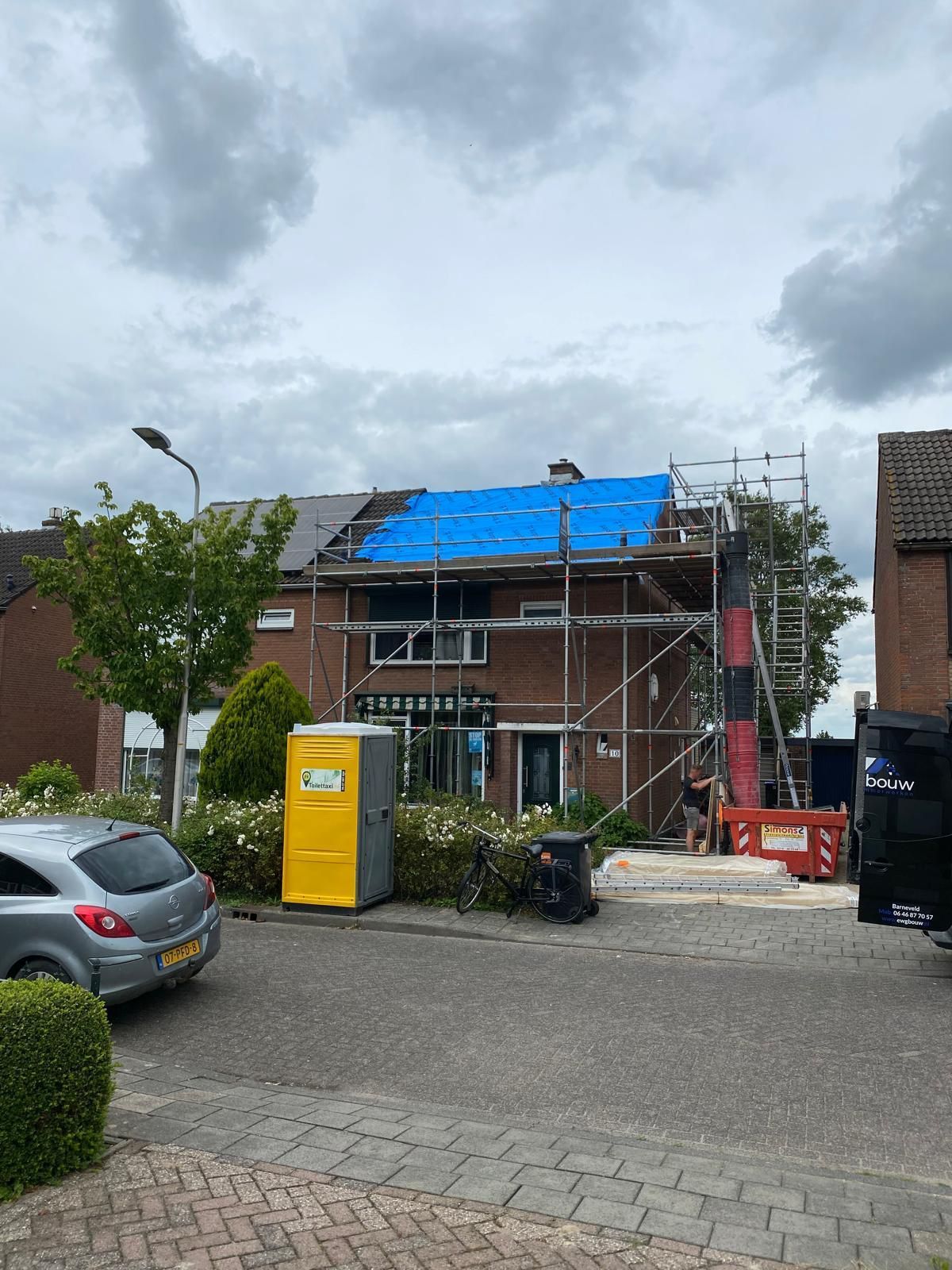 Dakrenovatie in uitvoering. Dakwerk met blauwe bedekking en constructie zichtbaar.
