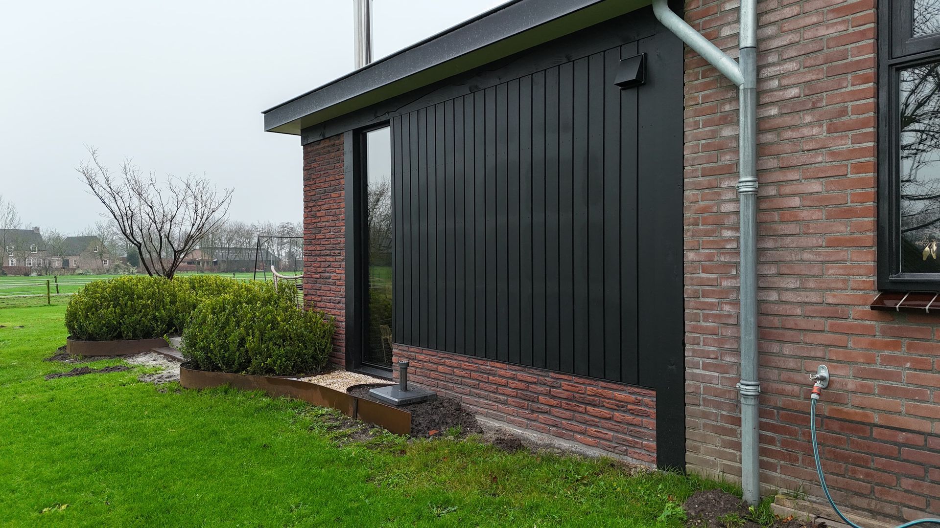 Moderne zwarte aanbouw aan bakstenen woning. Woninguitbouw en aanbouwwerk.