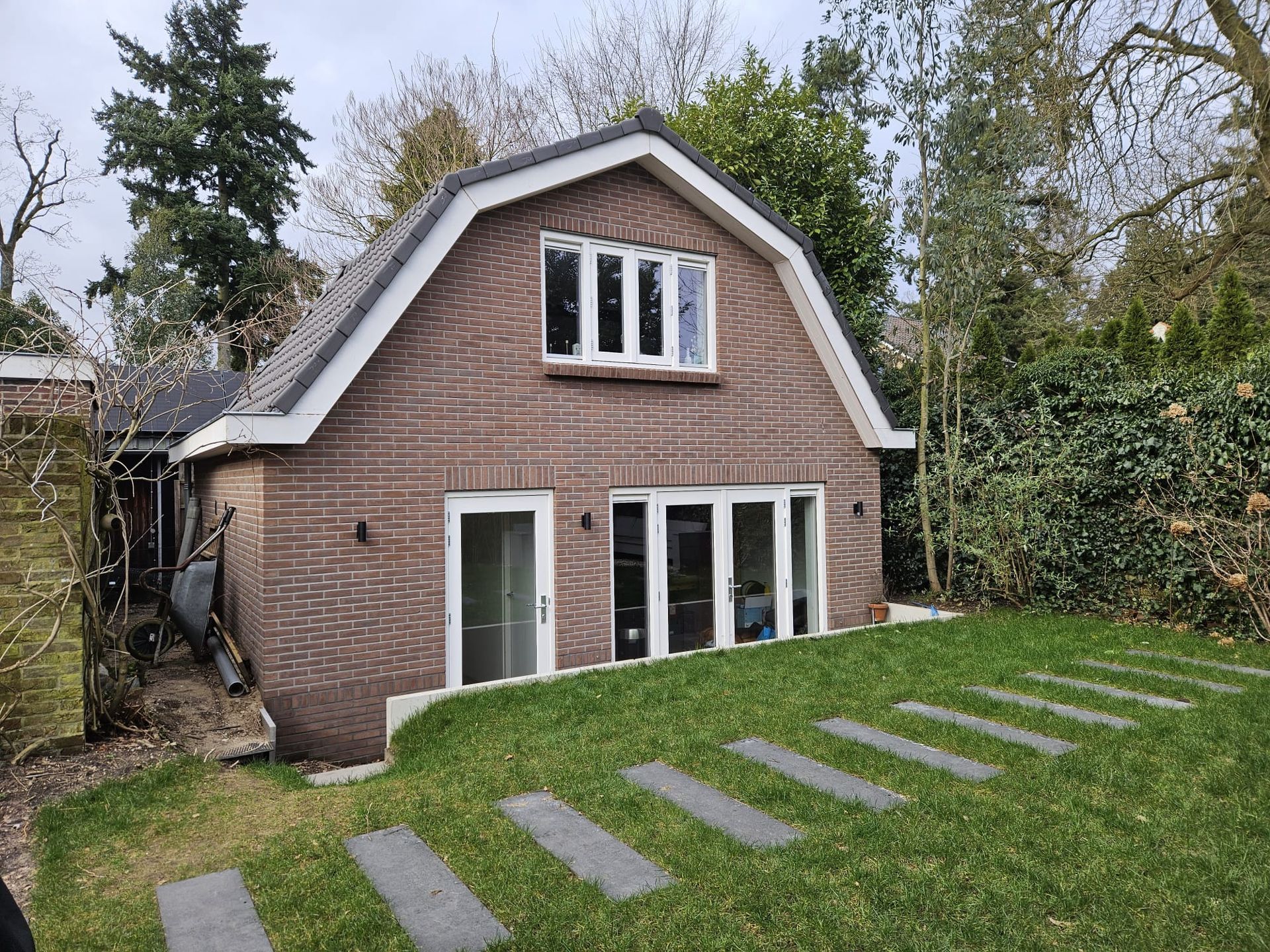 Bakstenen huis met wit omlijste ramen en een hellend gazon met stapstenen.