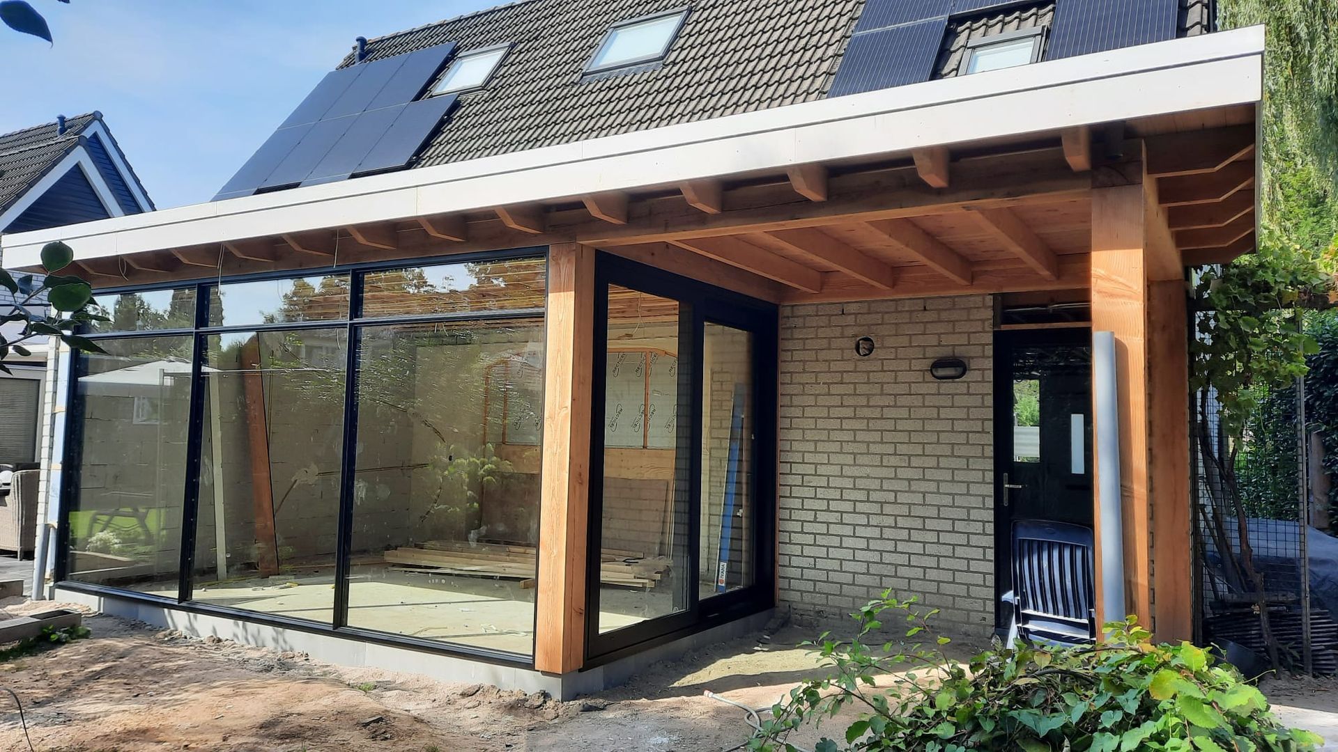 Moderne aanbouw met grote glazen ramen, bakstenen muren en een houten luifel in aanbouw.