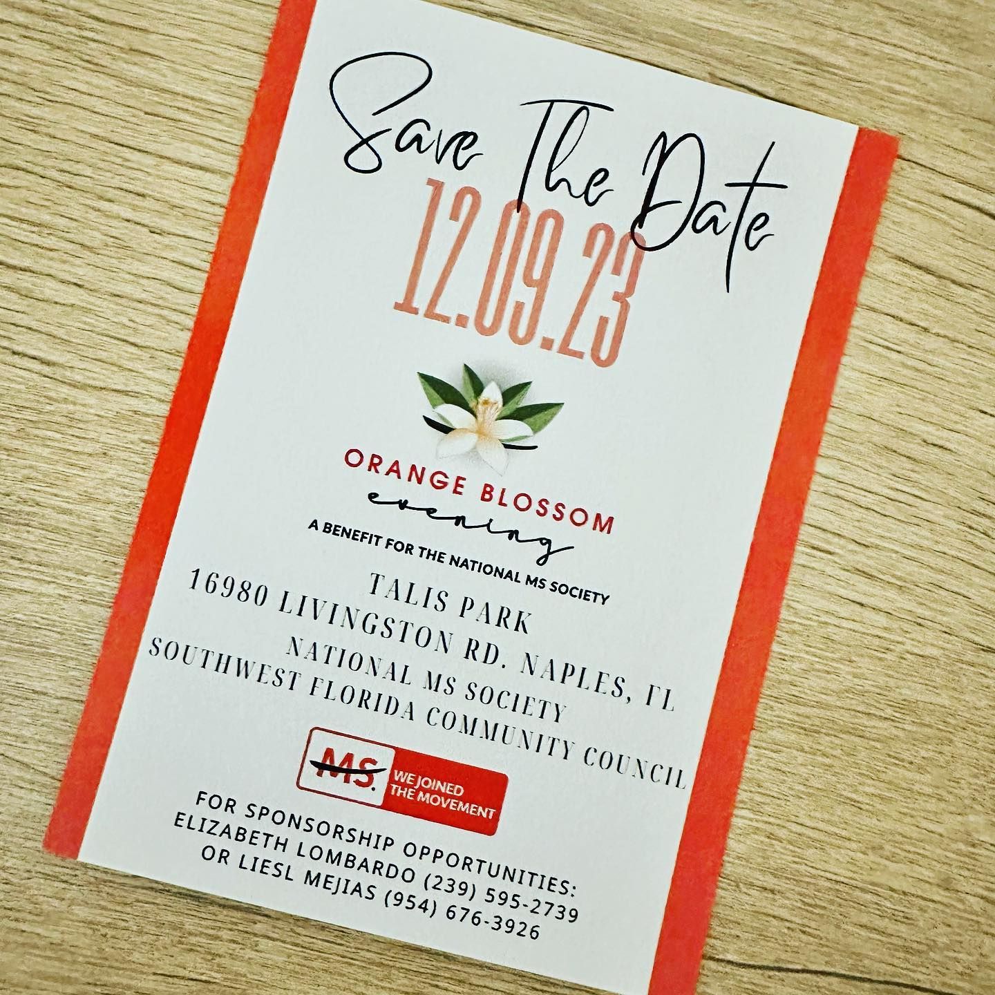 Orange-and-white “Save the Date” wedding card for 12.09.23 with floral details on a wooden surface