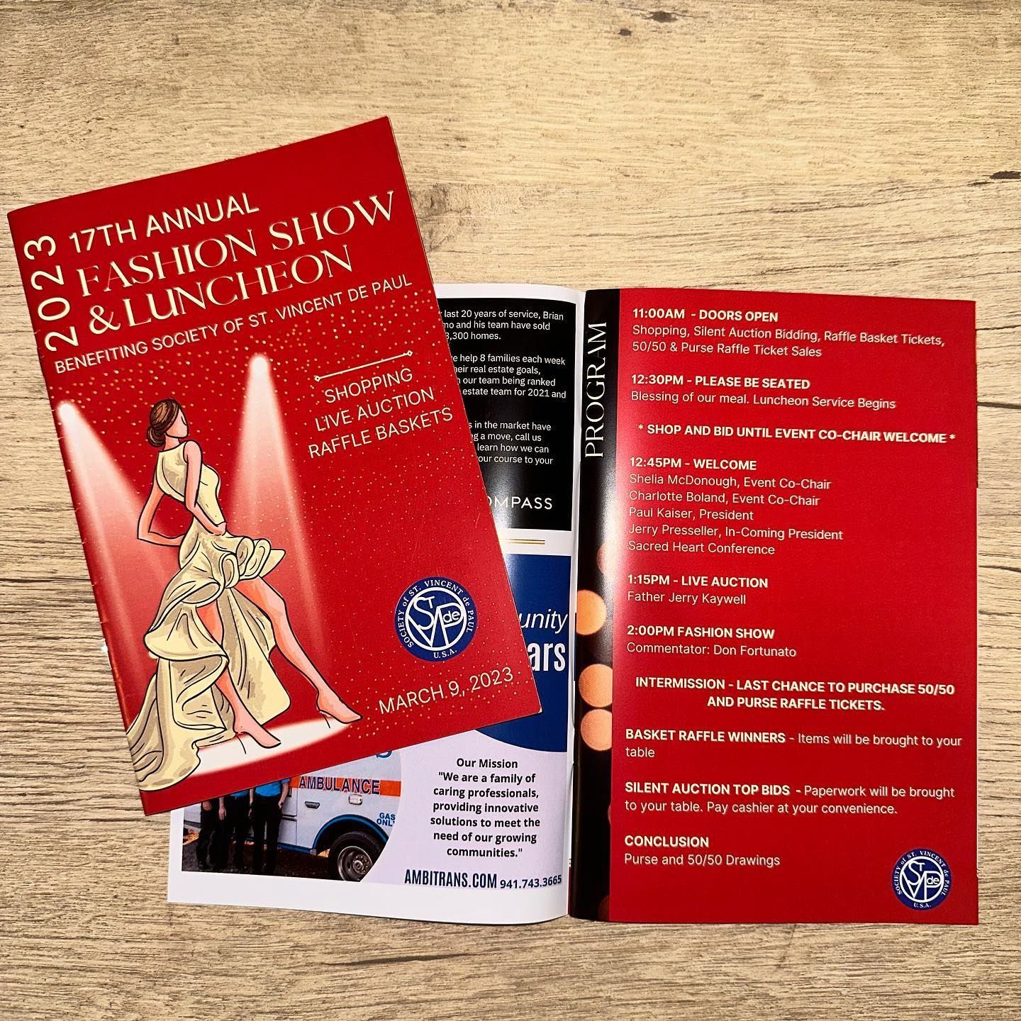Two red event brochures on a wooden table, one showing an illustrated figure and one with a program list.