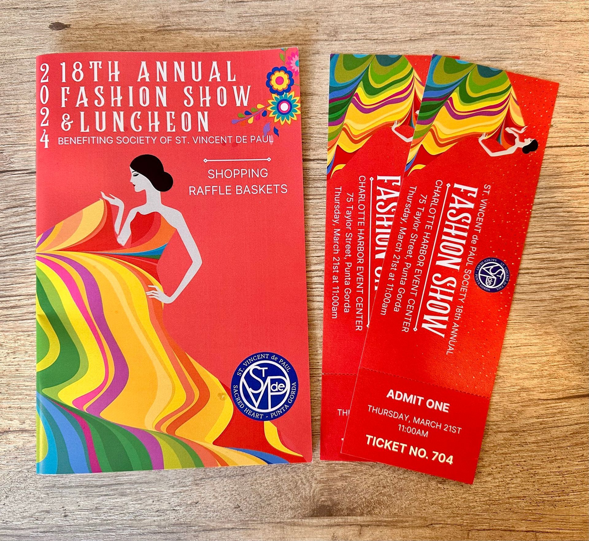 Two red fashion show and luncheon tickets with rainbow patterns on a wooden surface