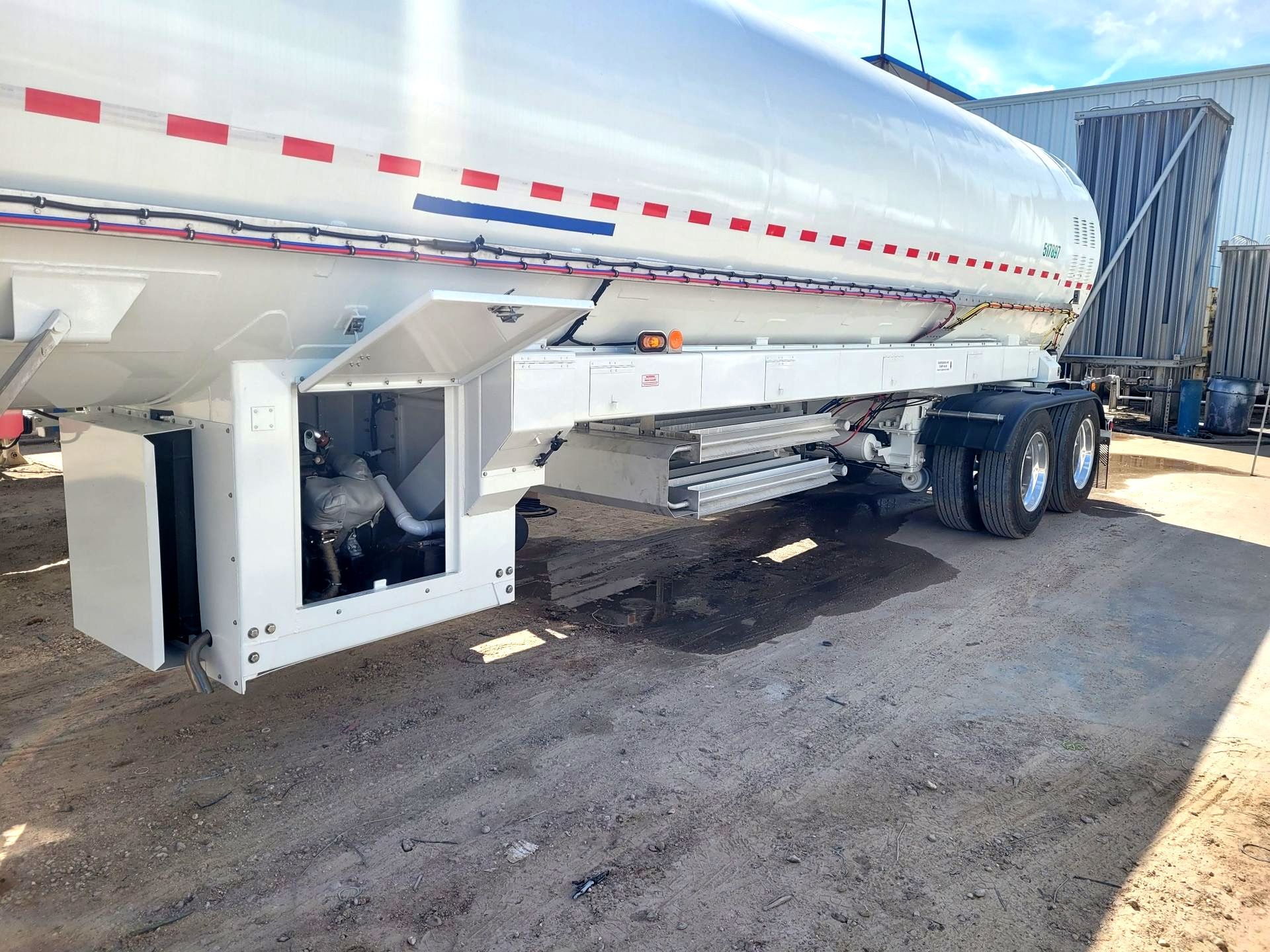 A white tanker truck is parked in a dirt lot.