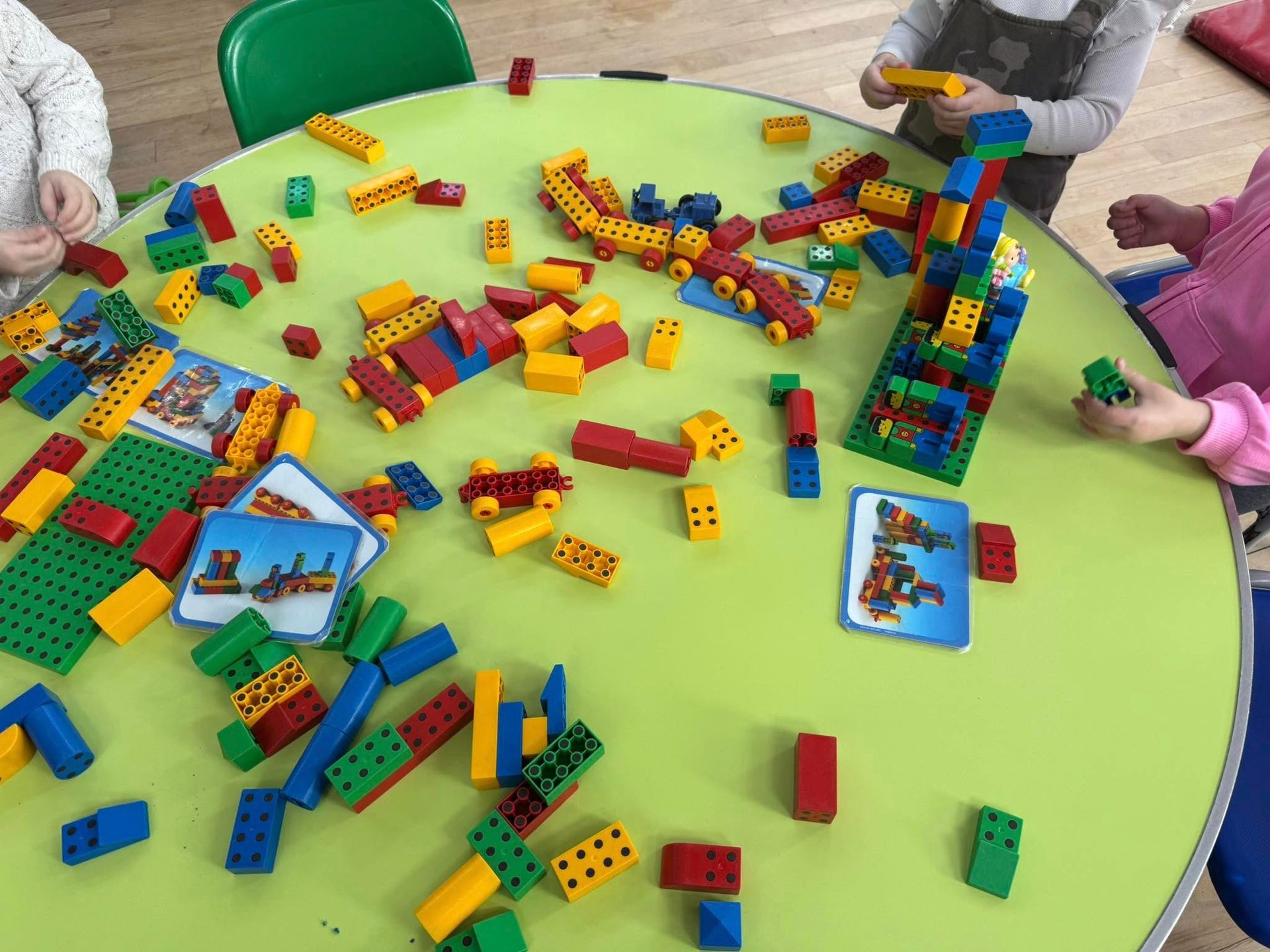 Children building with colorful Lego blocks on a green table.