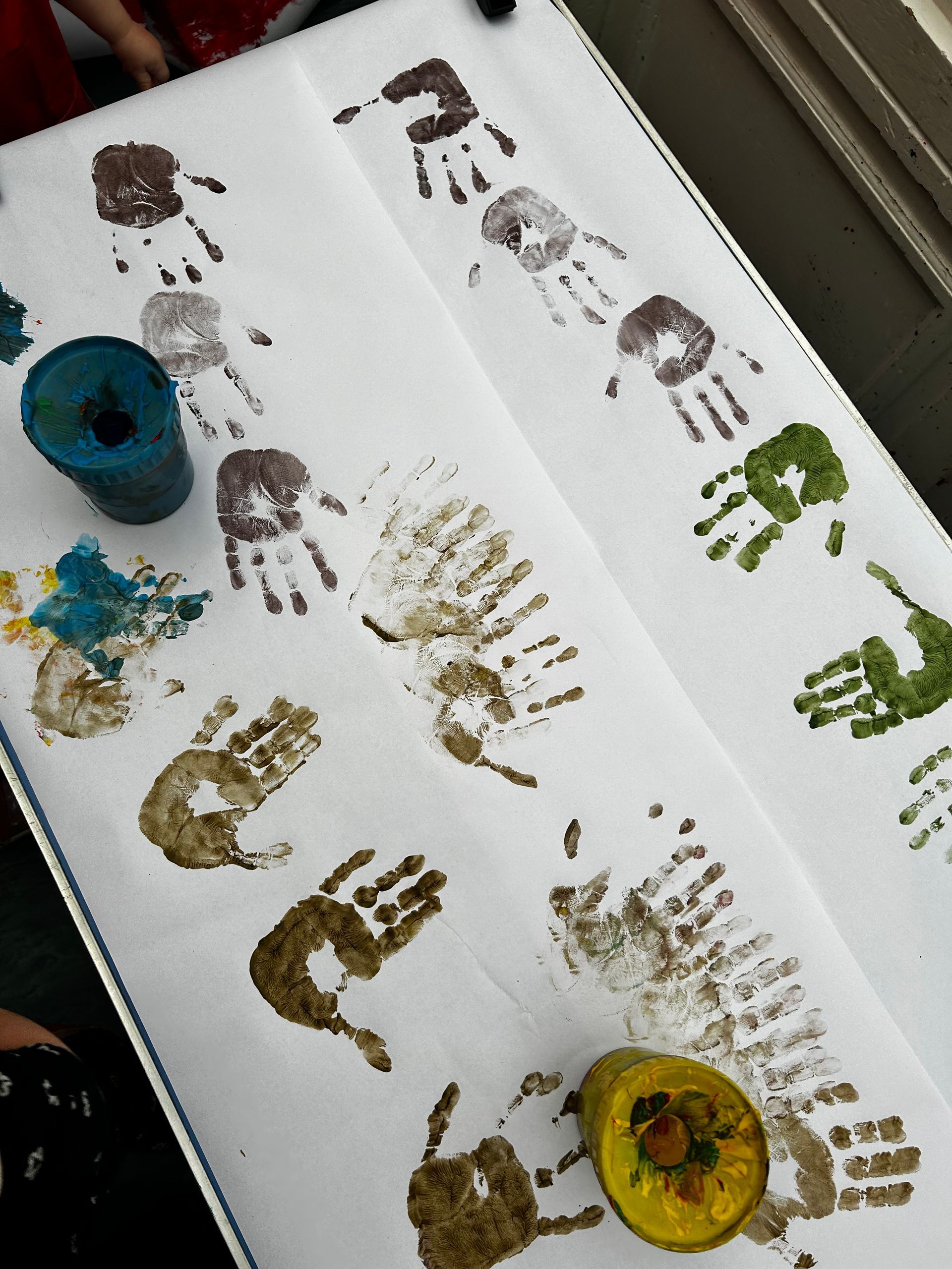 White paper covered in colorful handprints. Paint pots are visible near the prints.