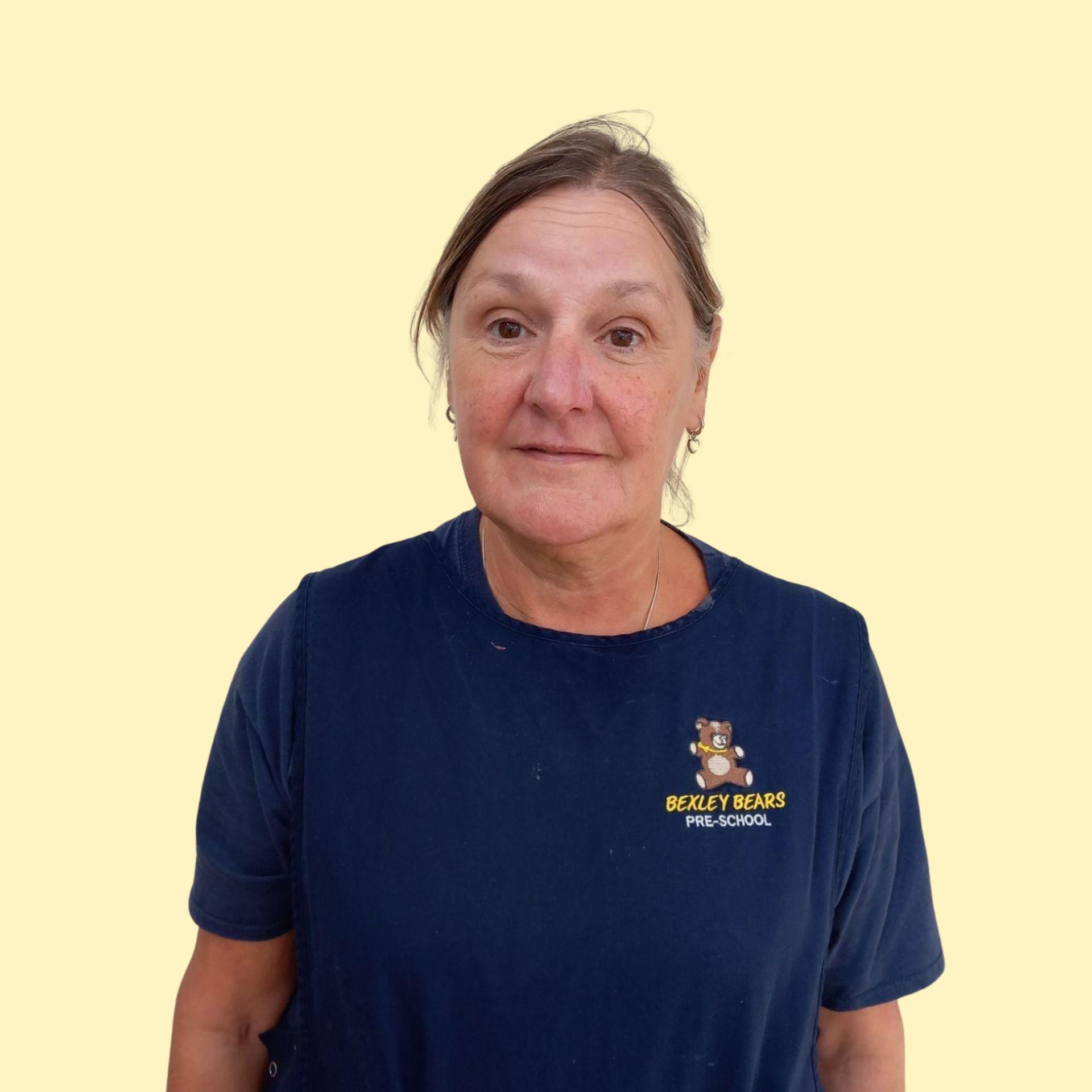 Blonde woman smiling broadly against a yellow background, wearing a white top.