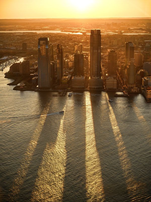 Golden sunset over a waterfront city skyline, with long shadows stretching across the water.