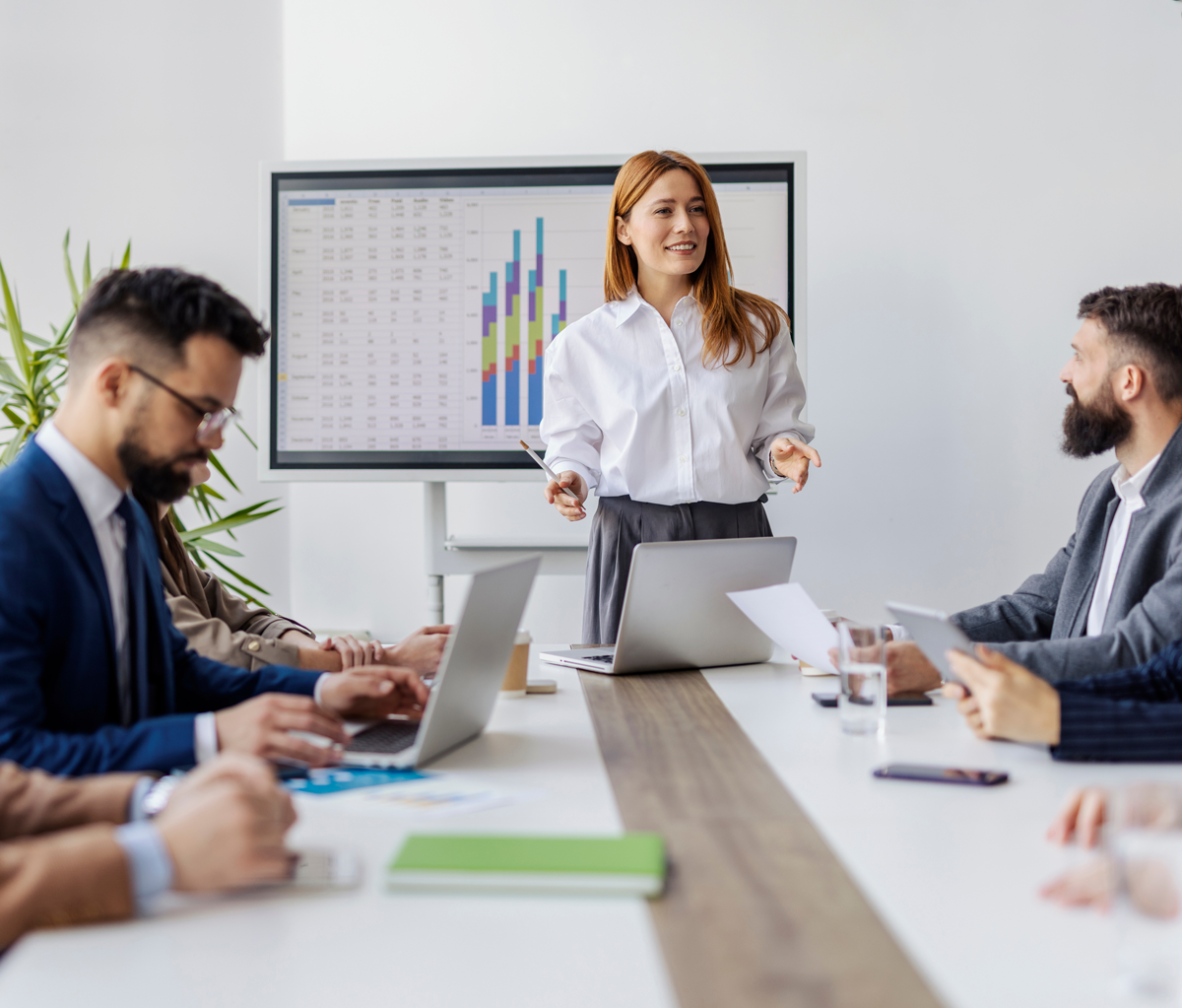 leadmonkey.ai | A woman is giving a presentation to a group of people sitting around a table.