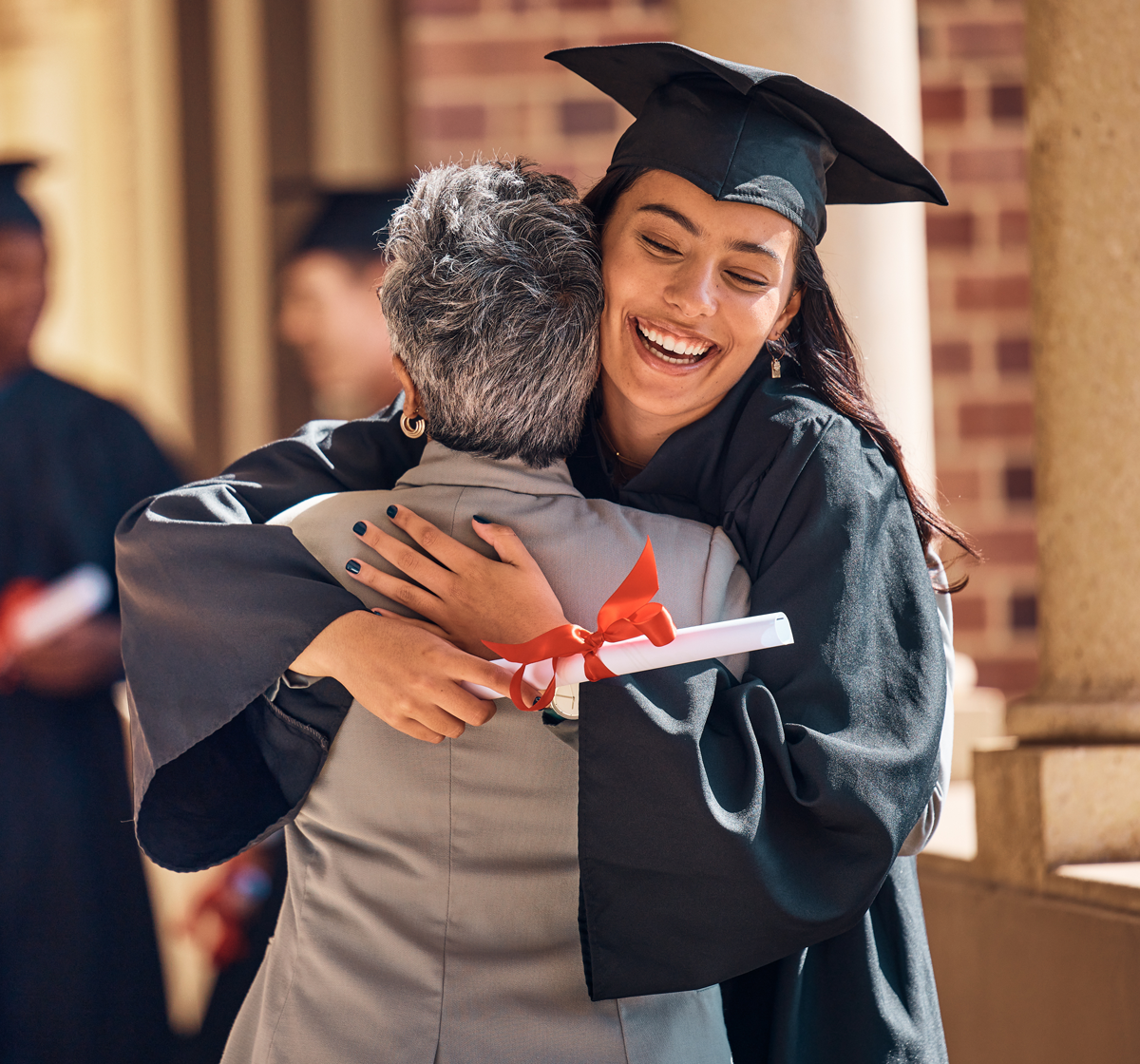 leadmonkey.ai | A woman in a graduation cap and gown is hugging an older woman.
