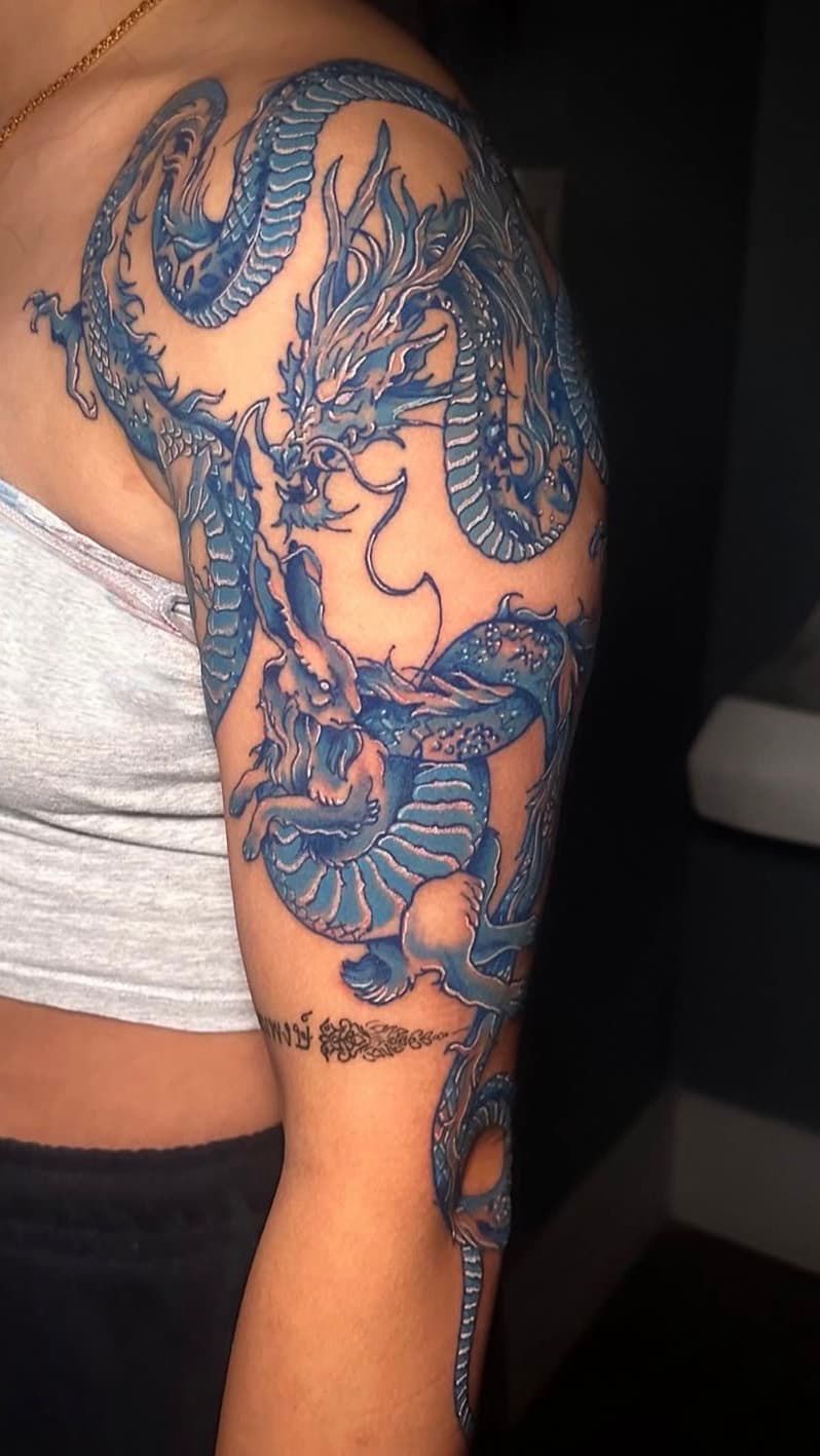 Arm with large blue dragon tattoo on shoulder and forearm against a dark background