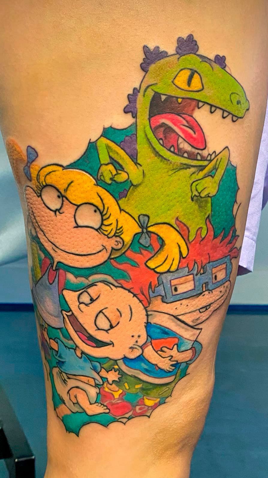 Colorful cartoon tattoo of Rugrats characters with a green reptile on a calf