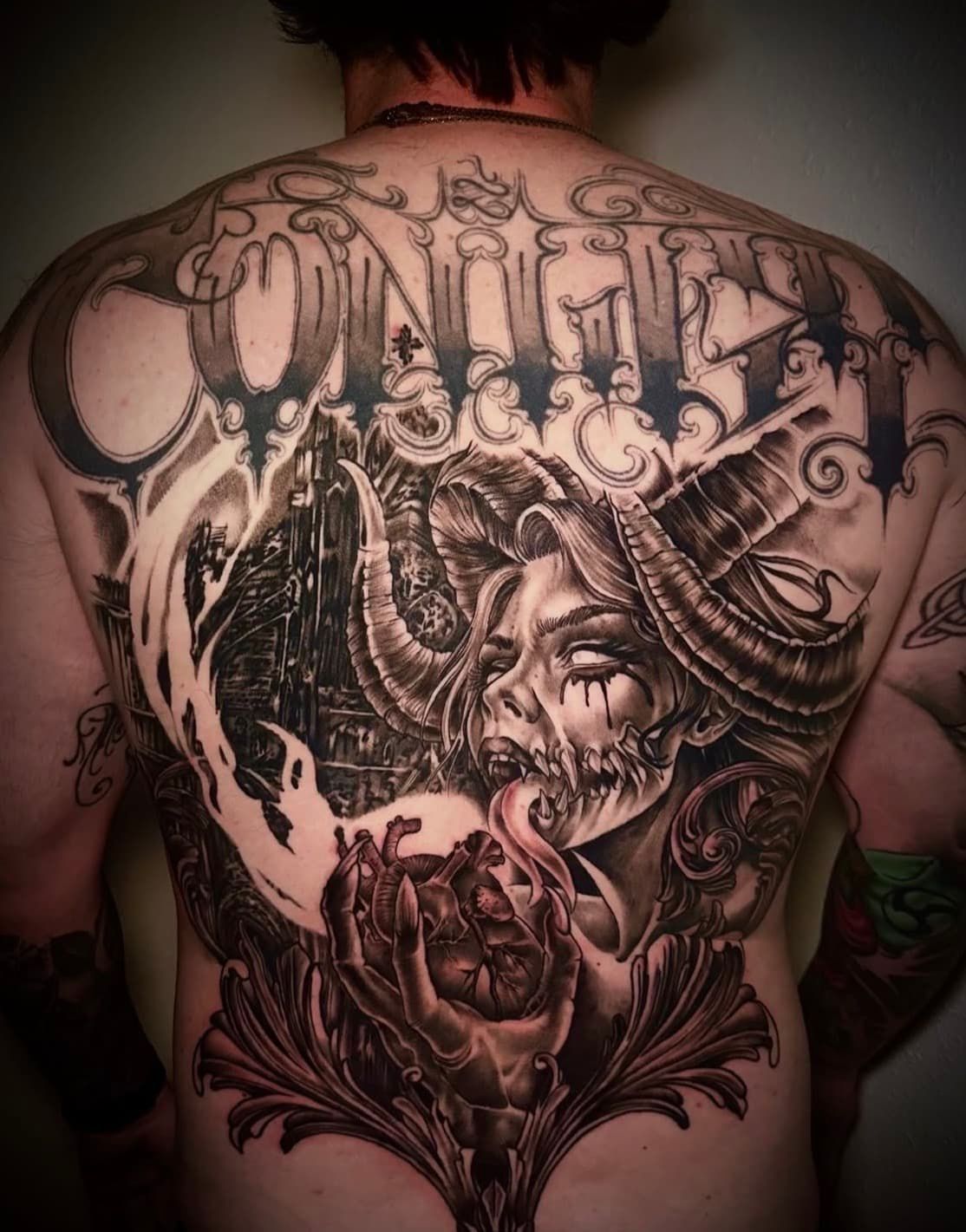 Back tattoo of an ornate black-and-gray surreal female face with swirling decorative patterns