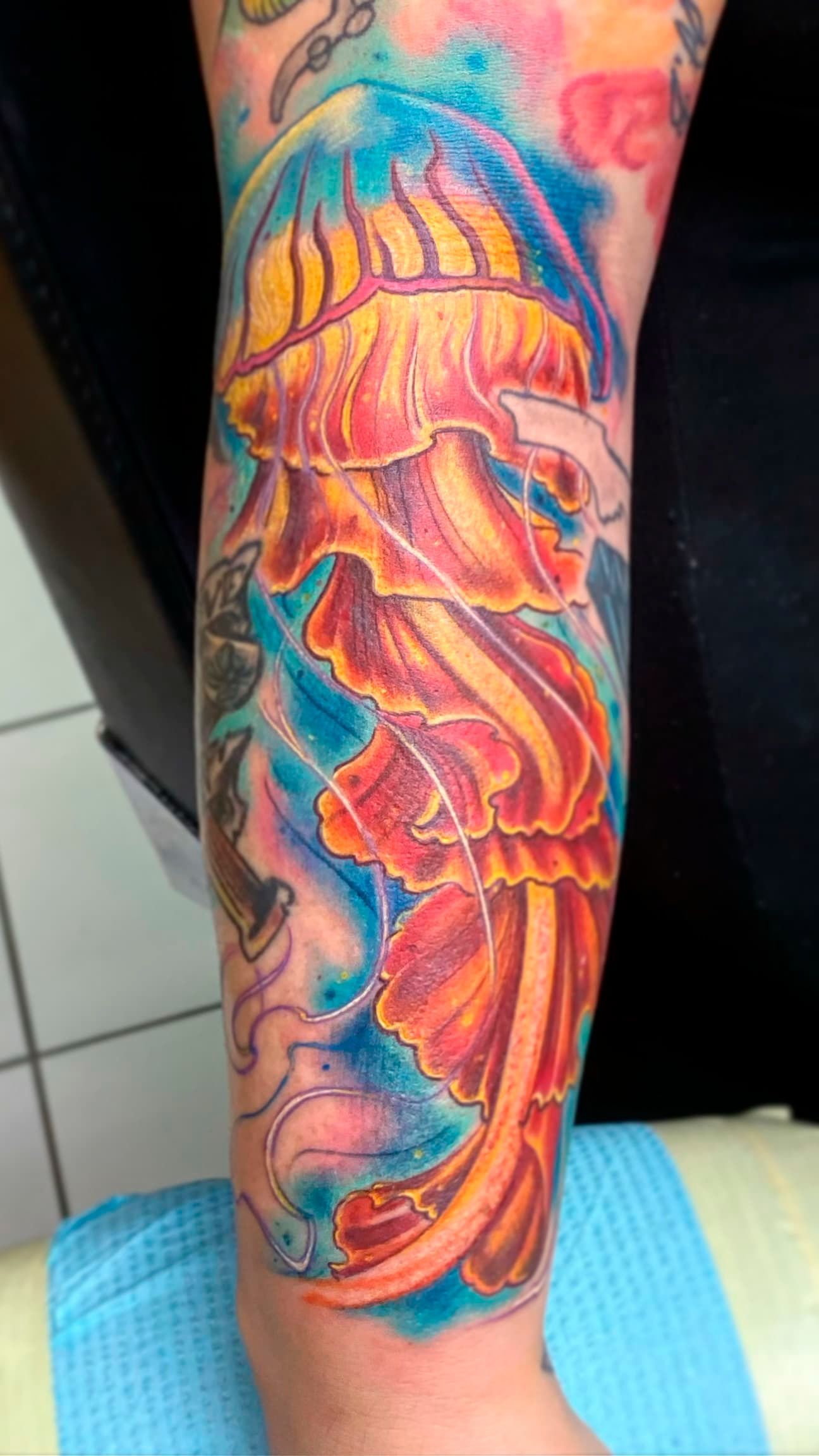 Colorful jellyfish tattoo on a lower leg, with vibrant pink, orange, blue, and yellow details