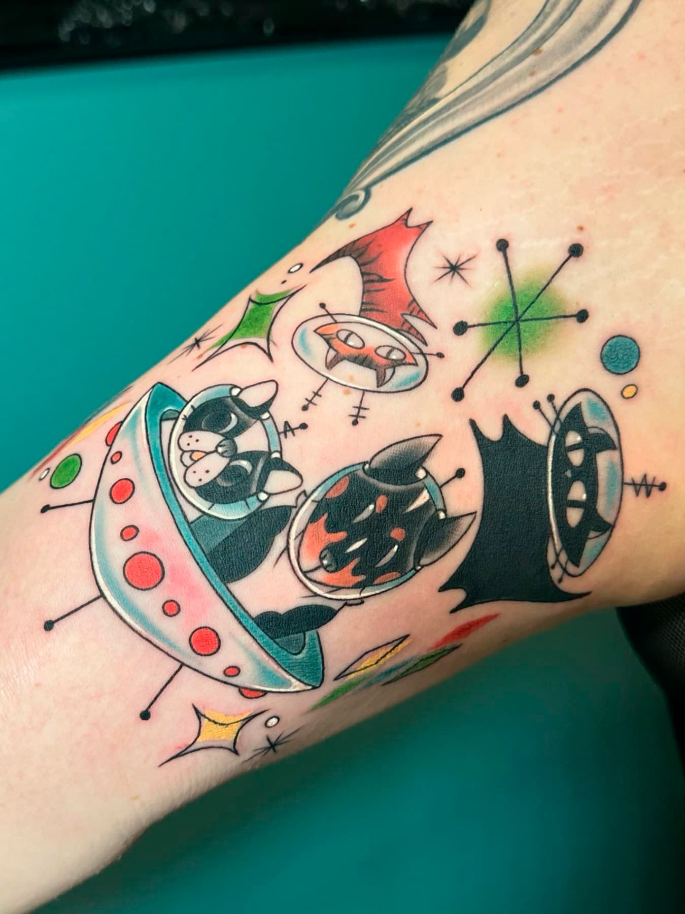 Colorful sci-fi tattoo on a forearm, featuring stars, planets, and a rocket ship.