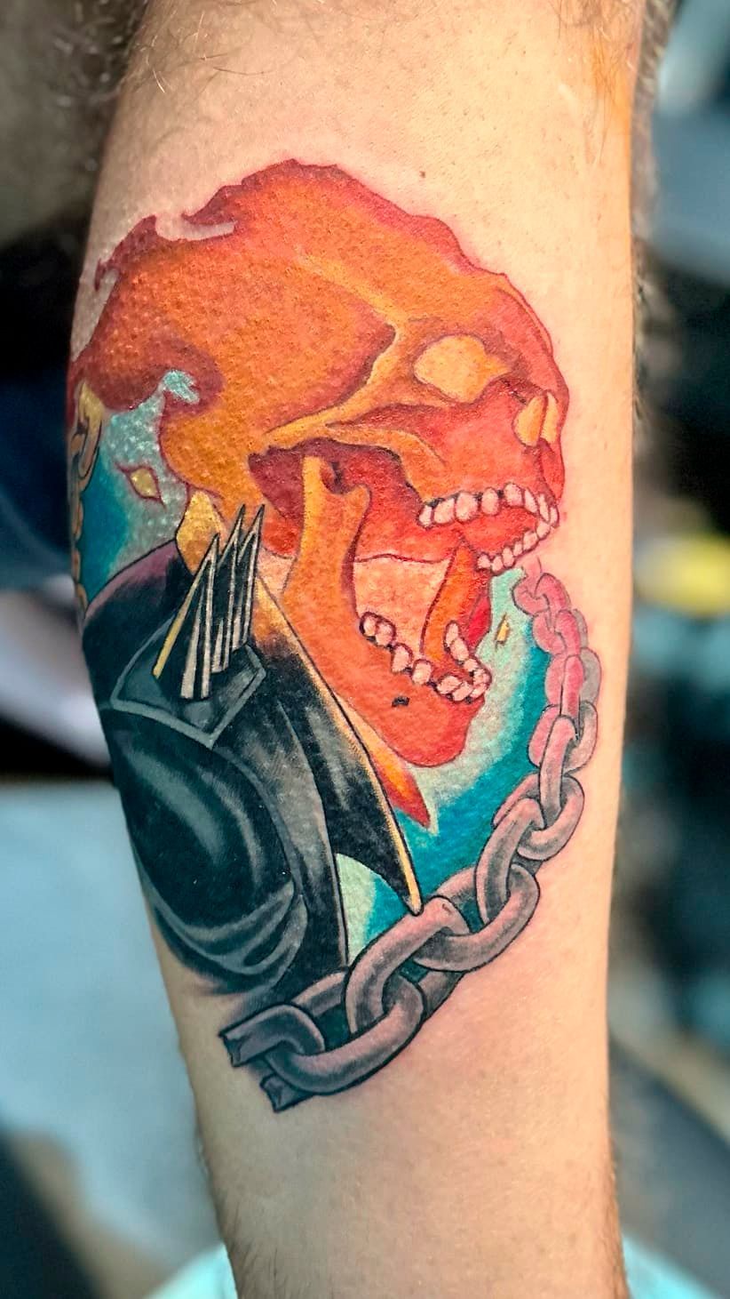 Colorful tattoo of a grinning skull in an orange hood with teal smoke on a forearm