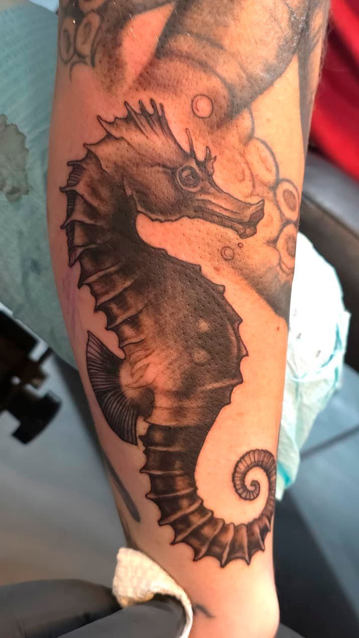 Black-and-gray seahorse tattoo on a person’s calf, with a curled tail and shaded details.