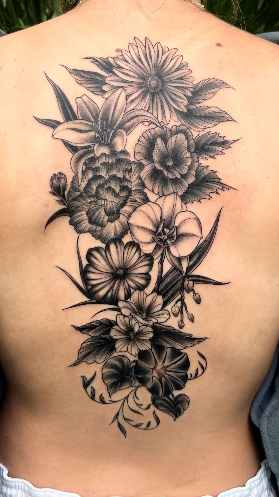 Black-and-gray floral tattoo vertically down a person’s upper back and spine