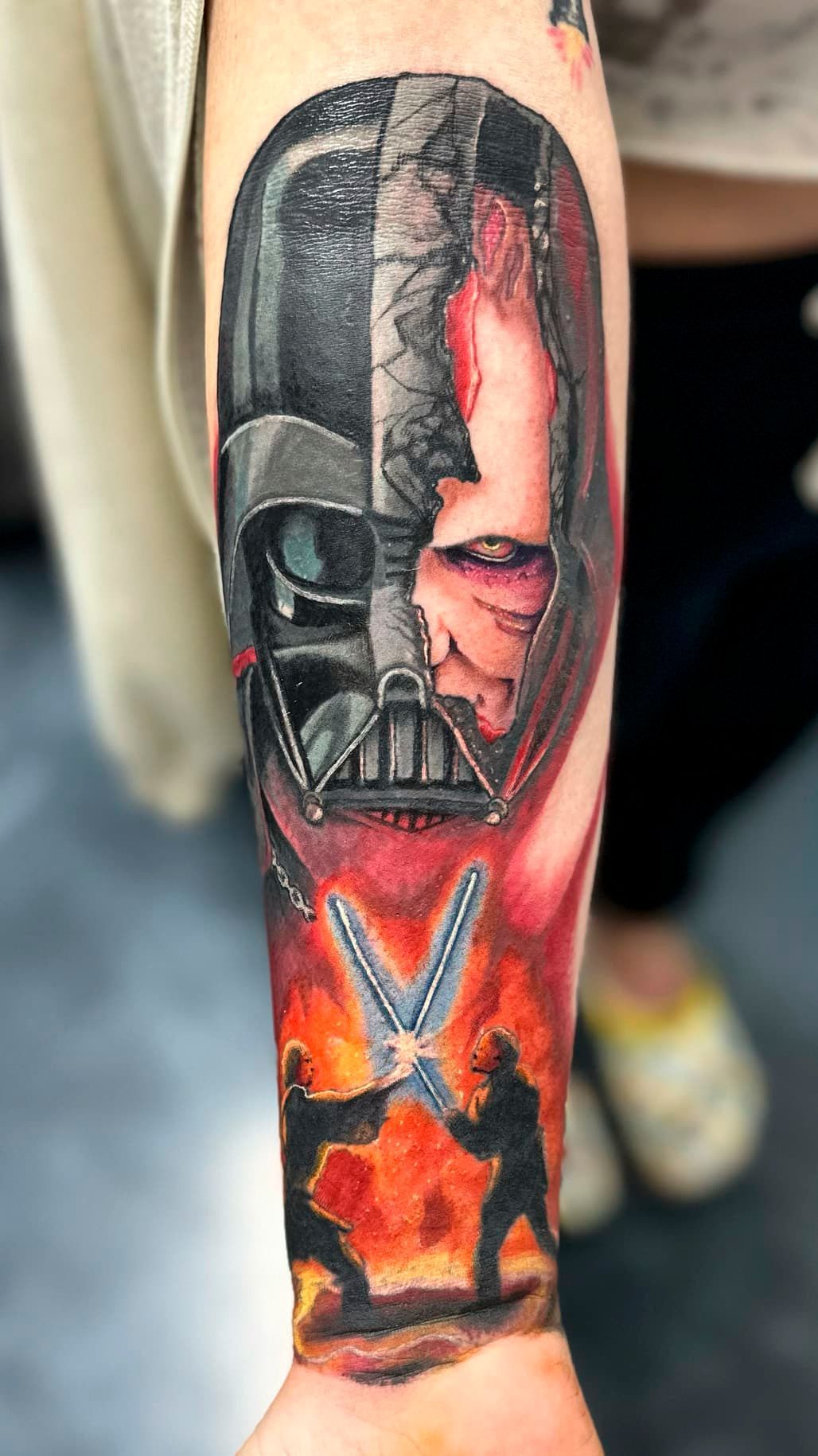Close-up of a forearm tattoo showing Darth Vader in black, red, and orange tones.