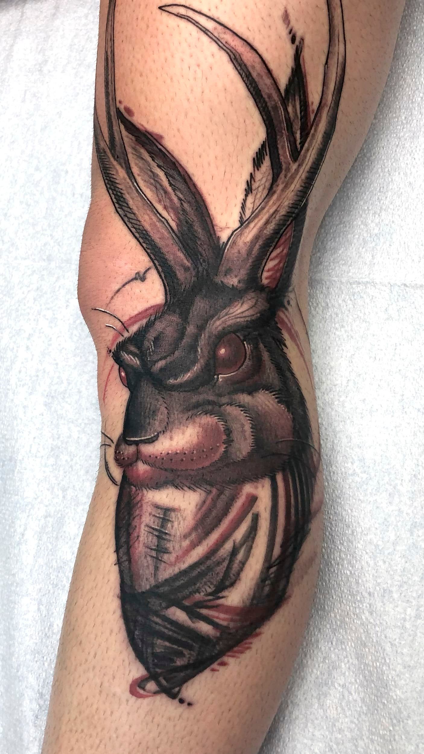 Black rabbit tattoo with long ears on a forearm, inked in dark shading with red accents.