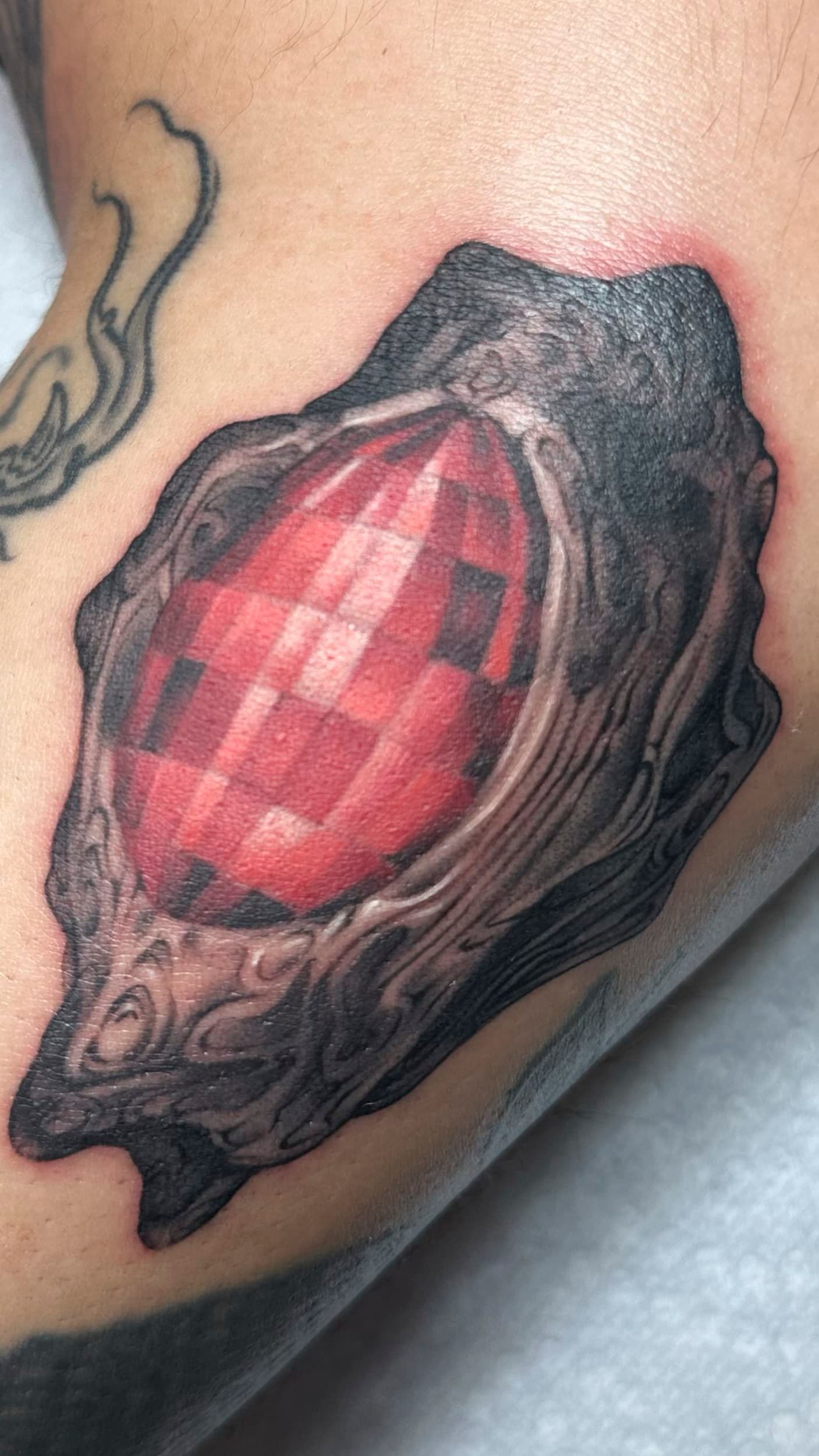 Close-up of a red faceted gemstone tattoo in a dark, organic black frame on skin