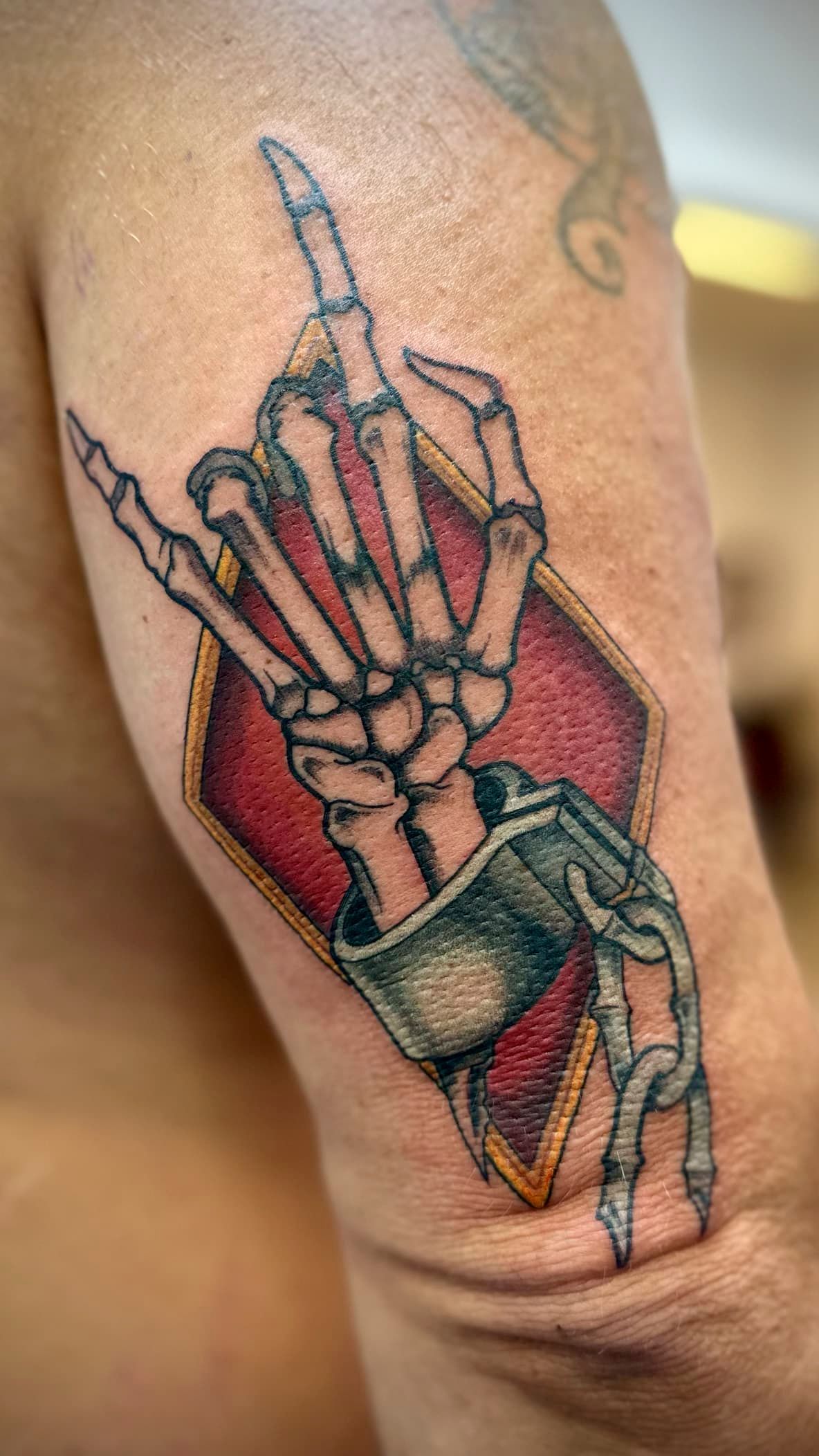 Skeleton hand tattoo making a middle finger gesture, with red and green accents on an arm