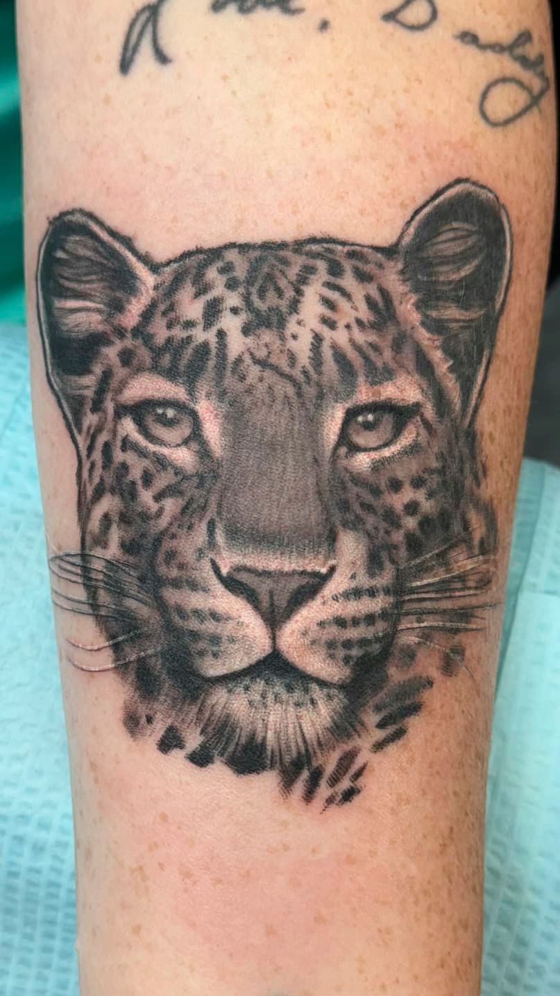 Black-and-gray leopard face tattoo on a person’s forearm or calf
