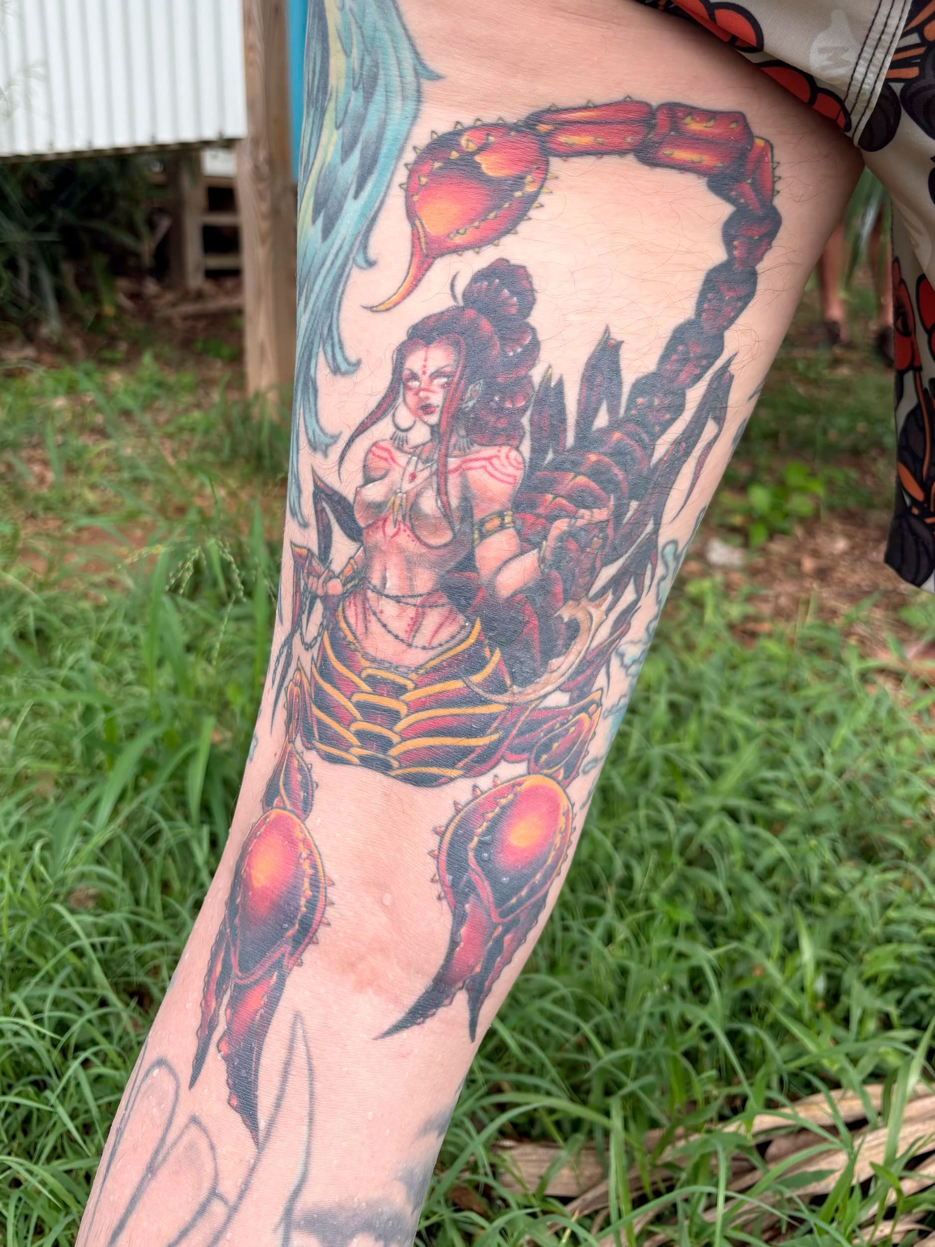 Colorful tattoo of a seated figure framed by orange-red flames on a lower leg.