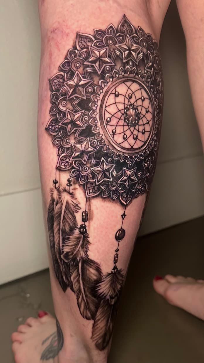 Close-up of an ornate black-and-gray dreamcatcher tattoo on a lower leg and foot.