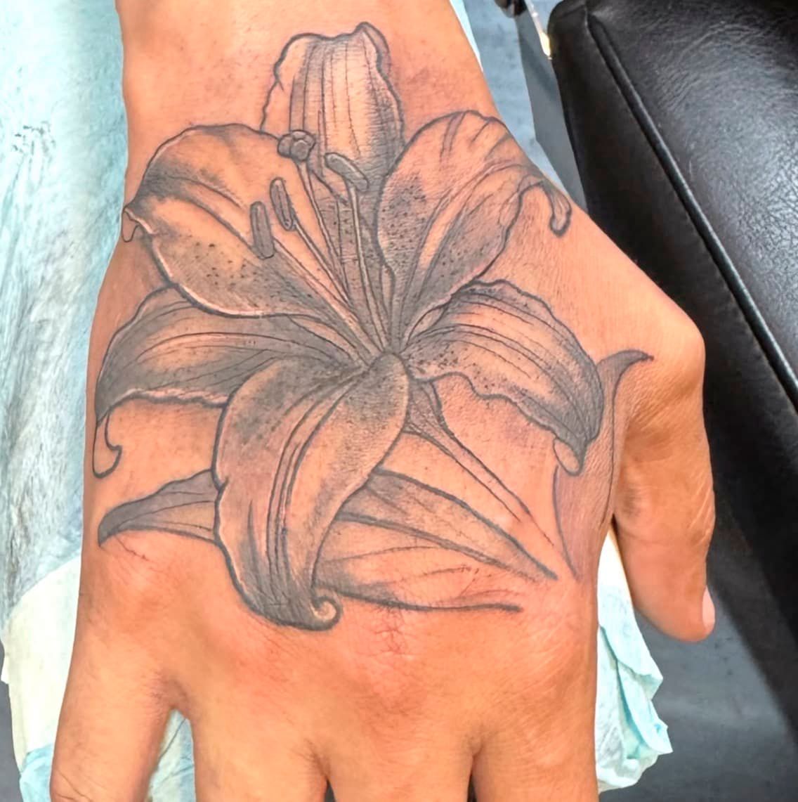 Close-up of a hand with a black-and-gray lily tattoo across the back of the hand