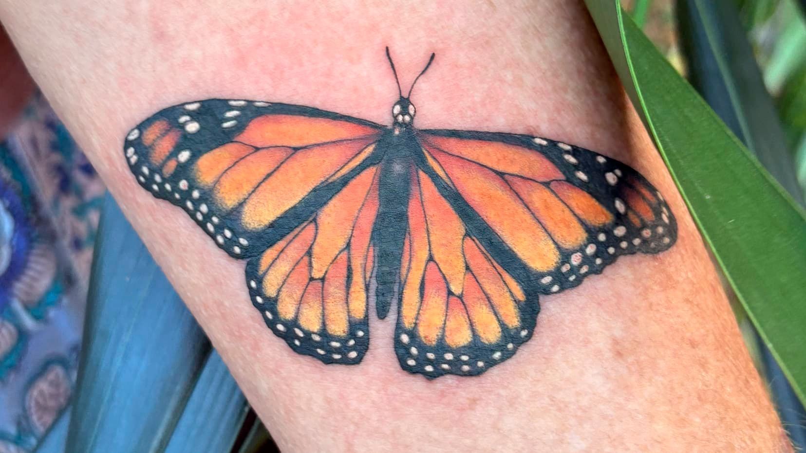 Orange and black butterfly tattoo on skin, wings spread