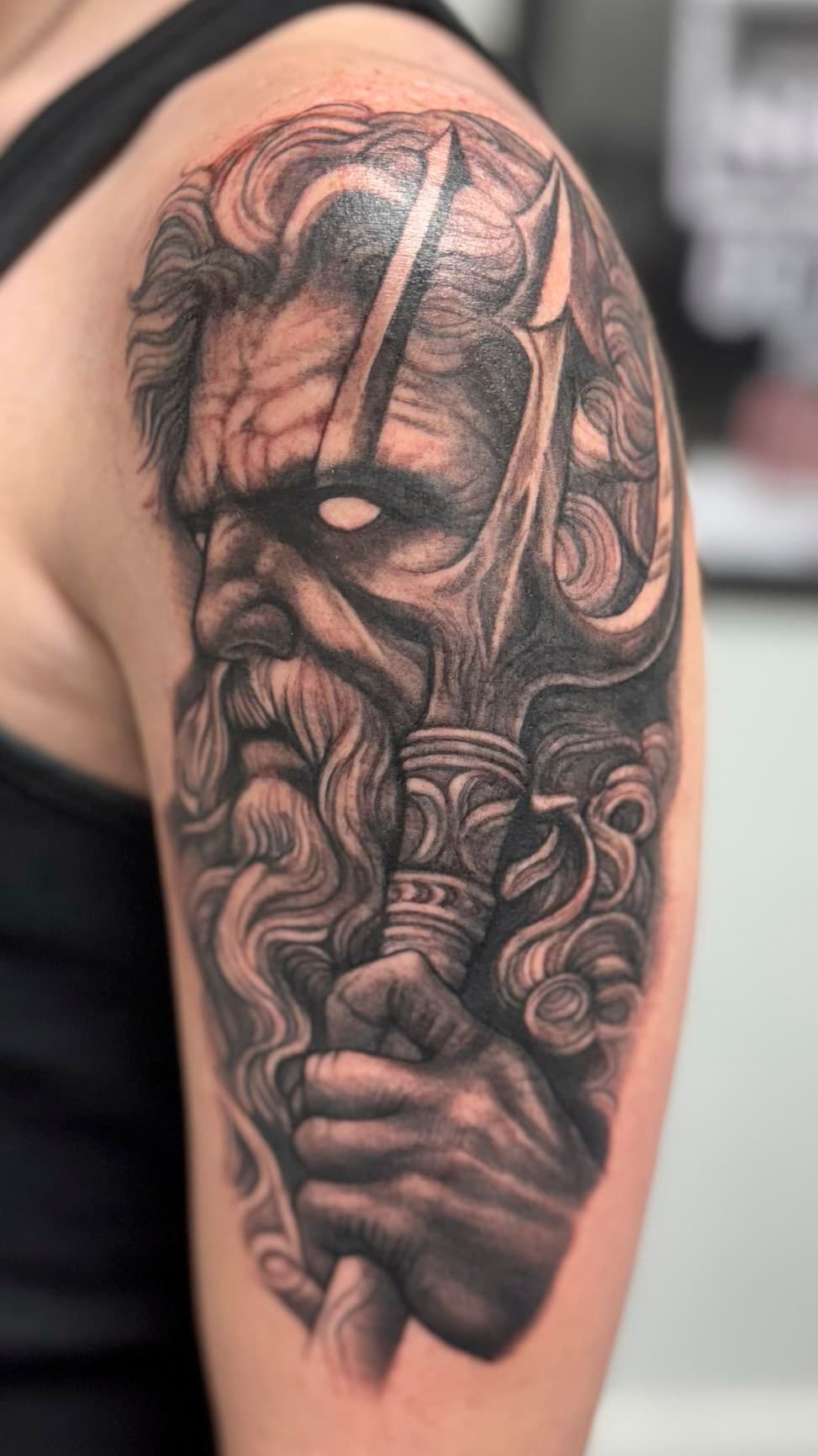 Black and gray tattoo of a bearded, intense face on an upper arm
