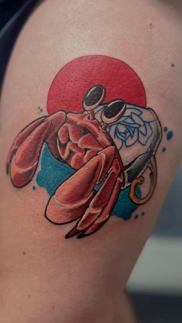 Hermit crab tattoo with red claws and blue shell on skin, backed by a red circle
