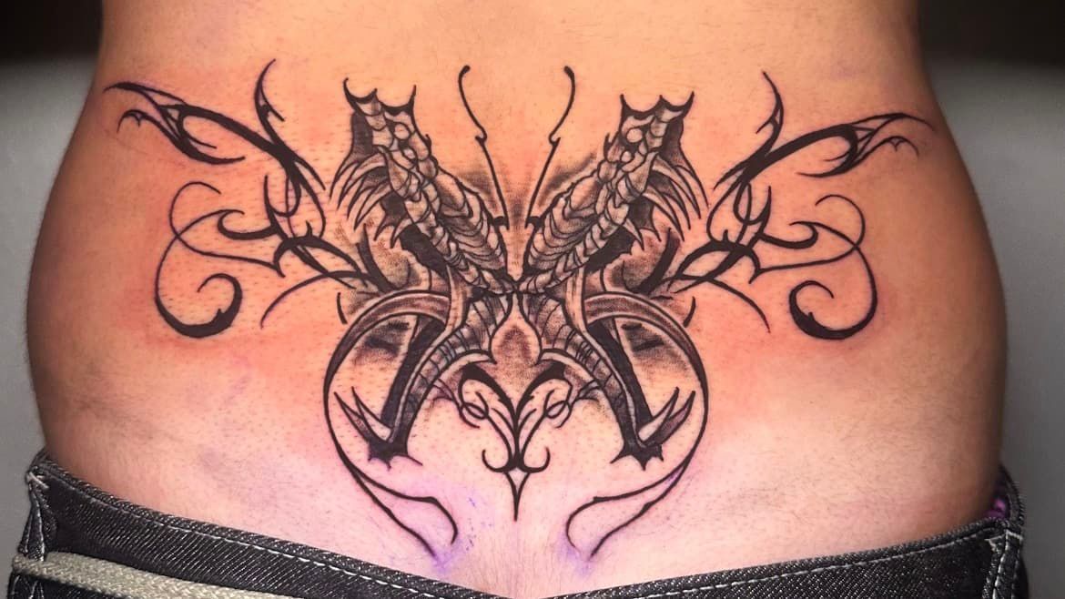 Black tribal tattoo across lower abdomen with mirrored winged designs and ornate swirls