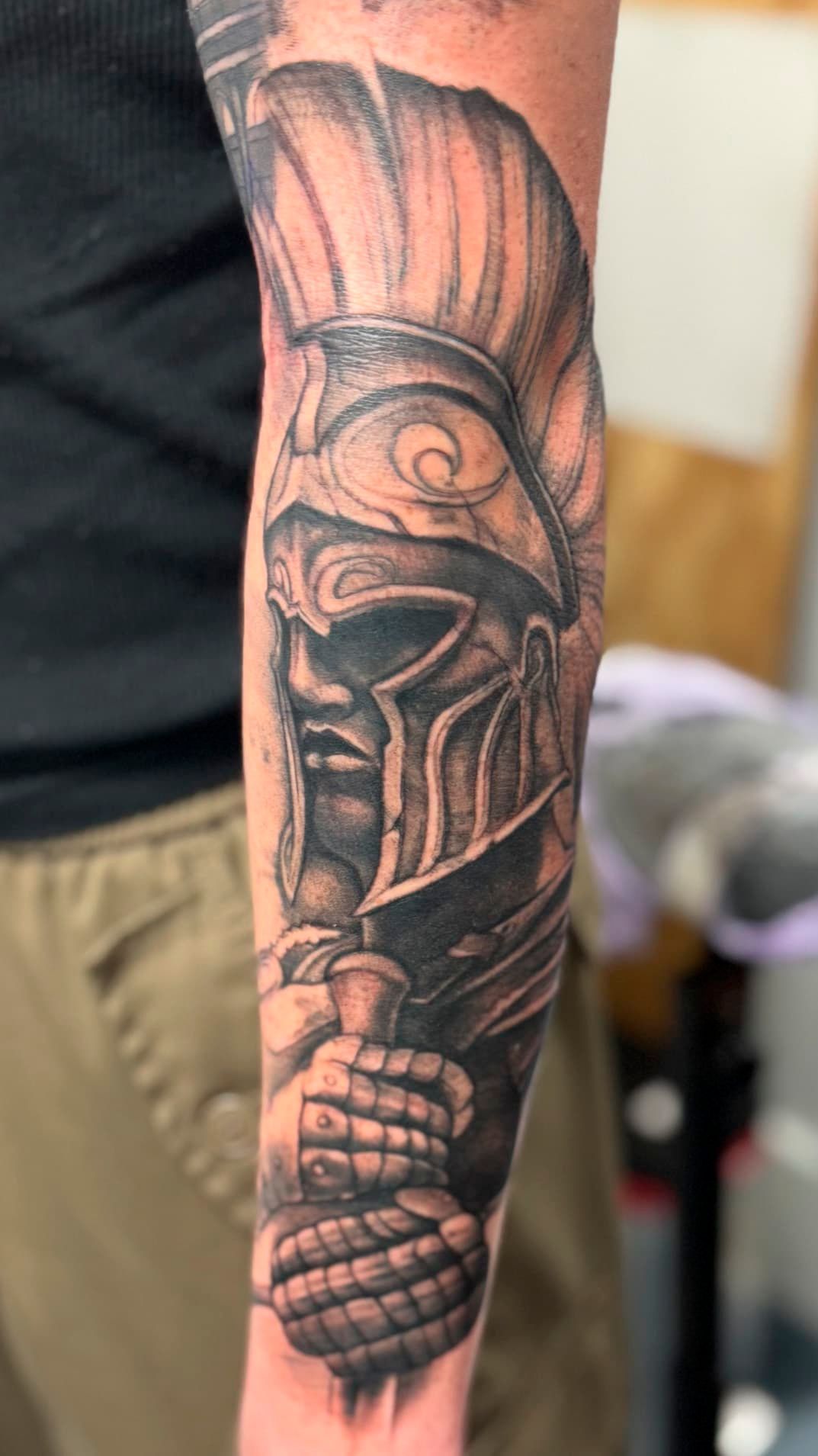 Close-up of a tattooed forearm with a dark tribal helmet design in black ink
