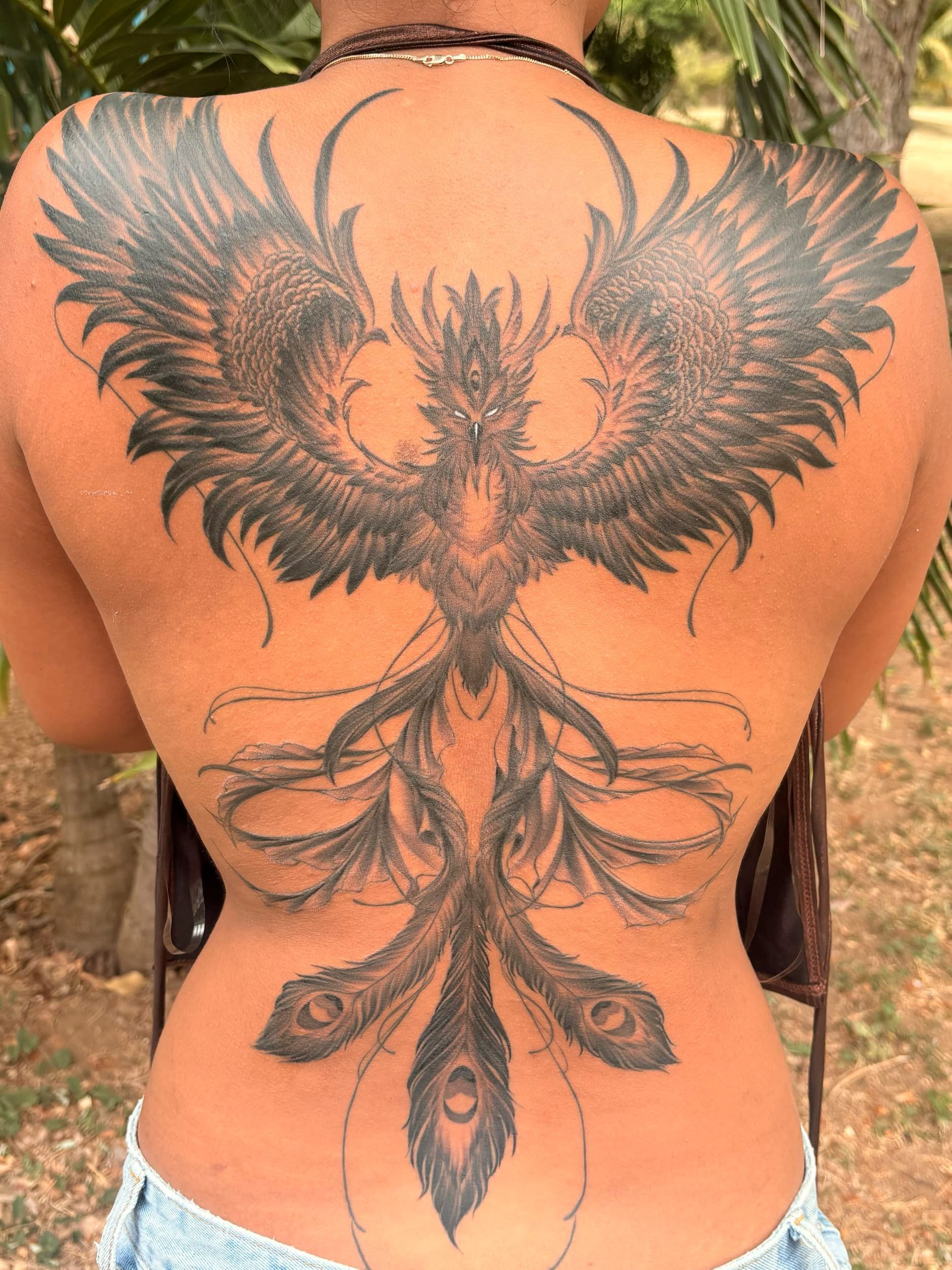 Back tattoo of a detailed black-winged bird with flowing ribbon-like feathers on a person's upper and lower back