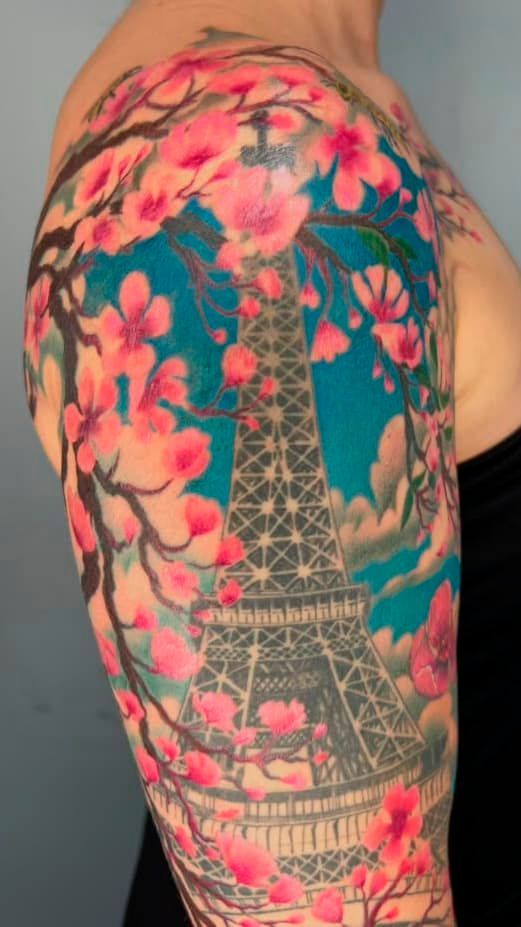 Eiffel Tower tattoo with pink flowers and green leaves on a shoulder and upper arm