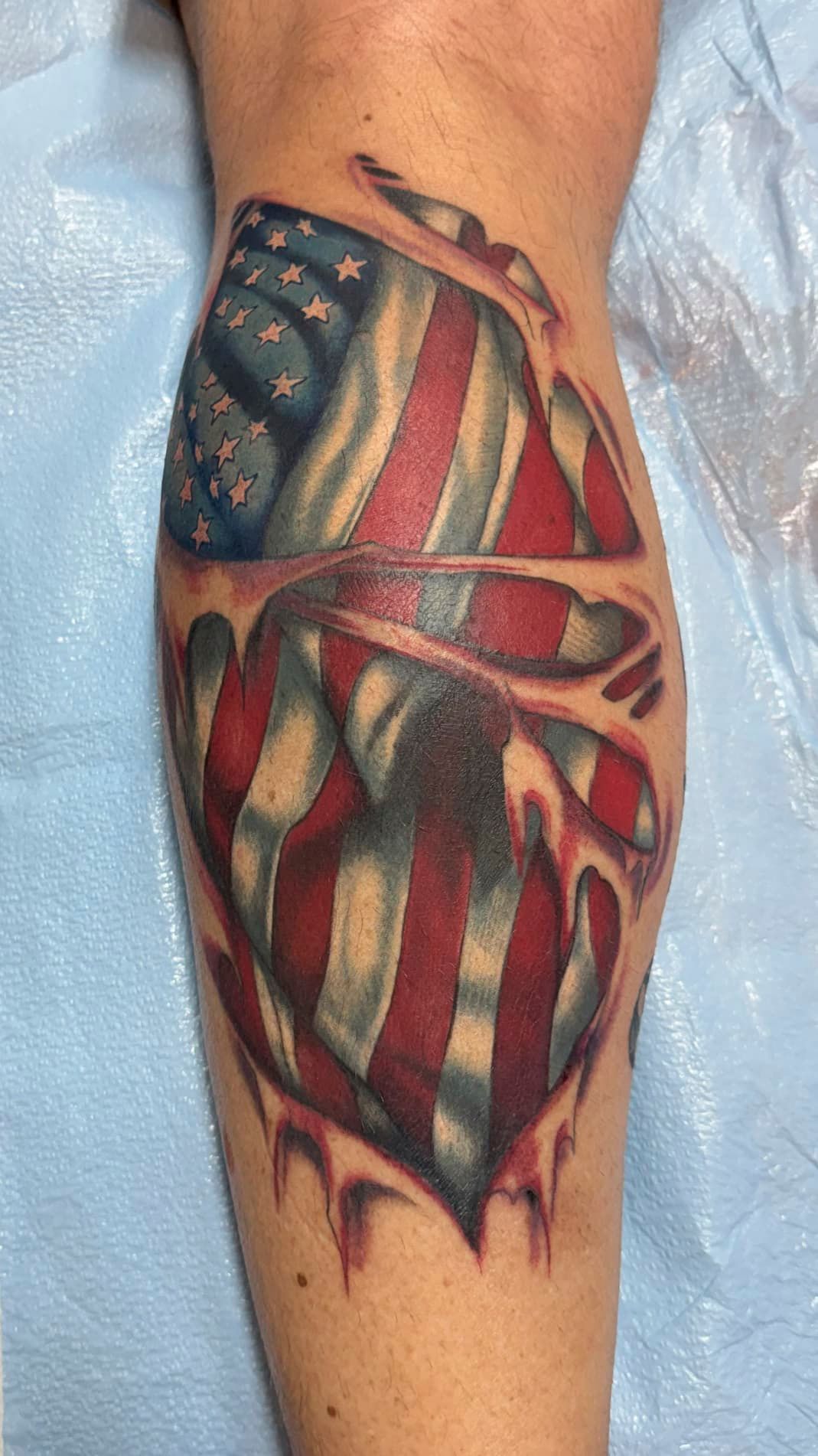 Tattooed forearm with a colorful American flag-inspired design and red abstract accents