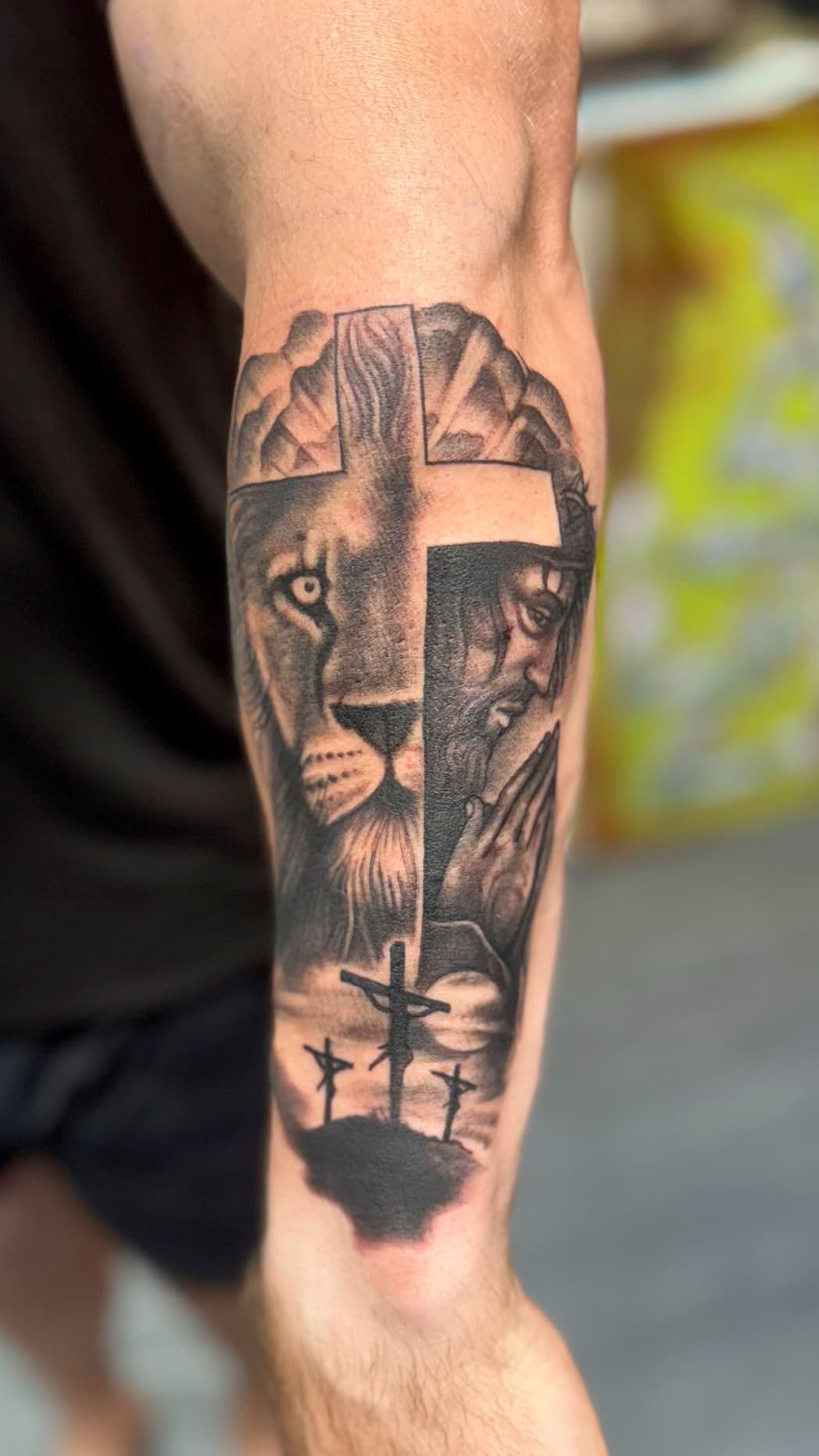 Lion tattoo in black and gray on a person’s calf, with geometric patterns and a cross at the bottom