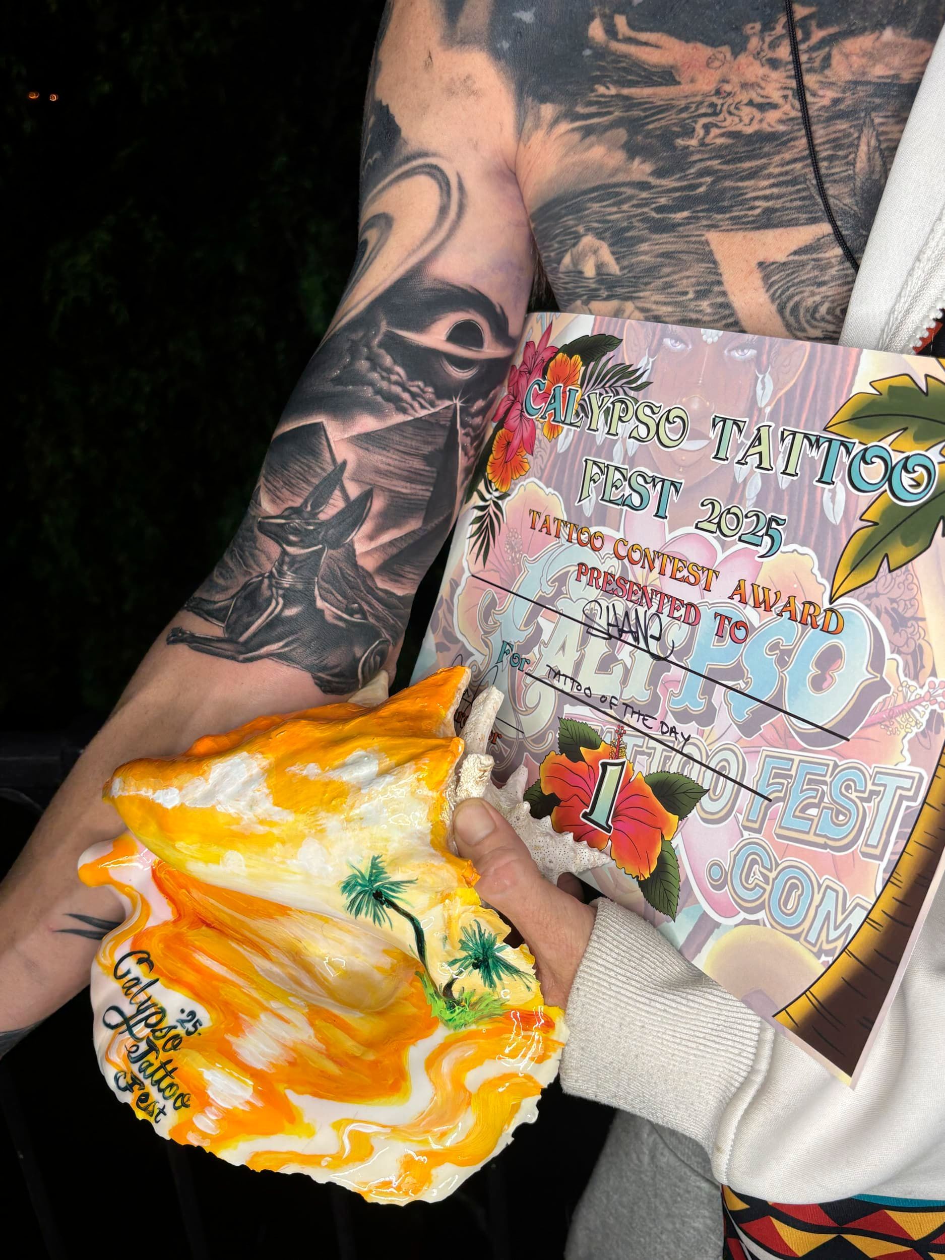 Person holding a wrapped dessert and a pastel card, with a tattooed arm visible